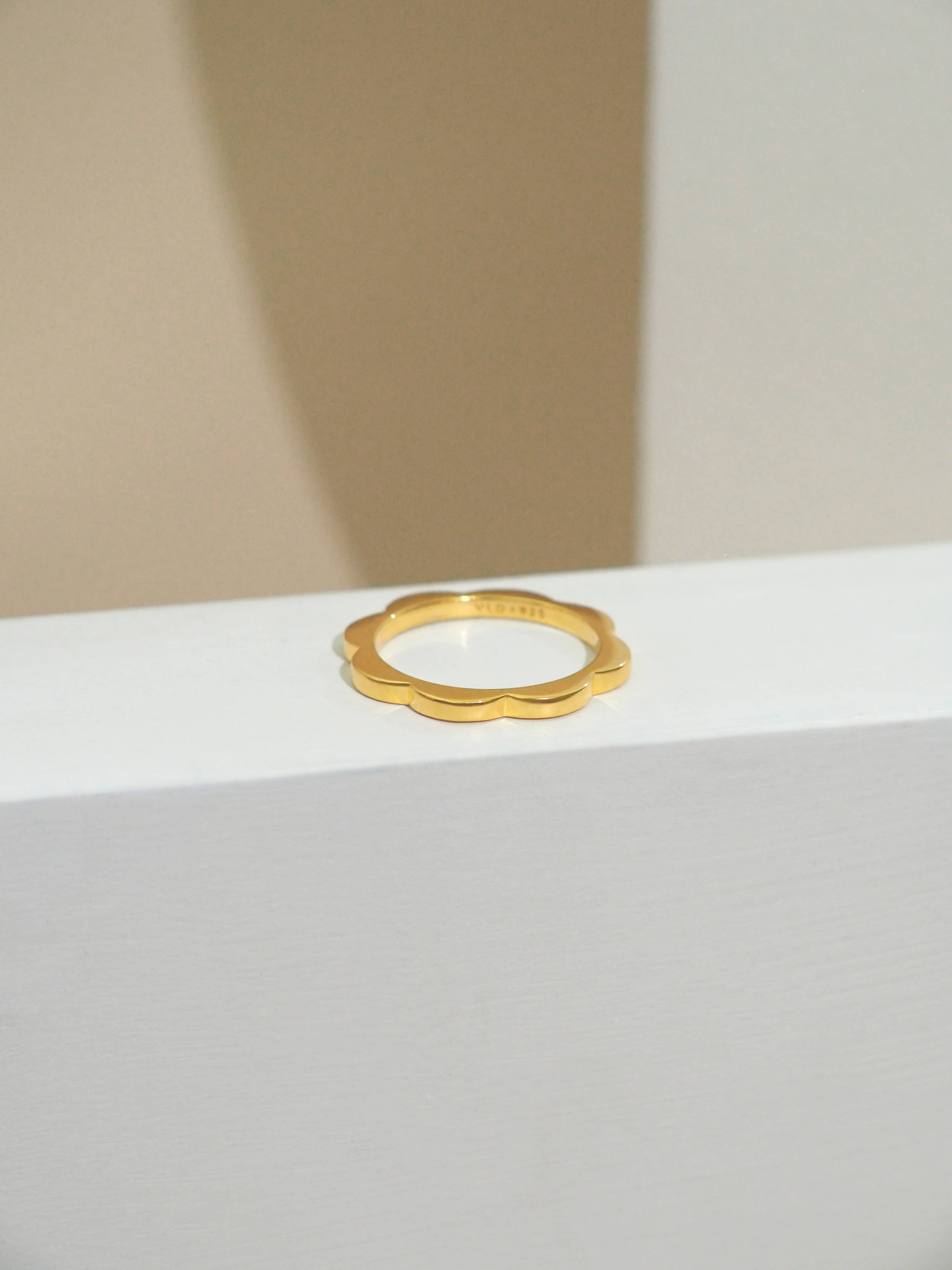 A minimal gold-plated stacking ring with a flower design placed on natural color background.
