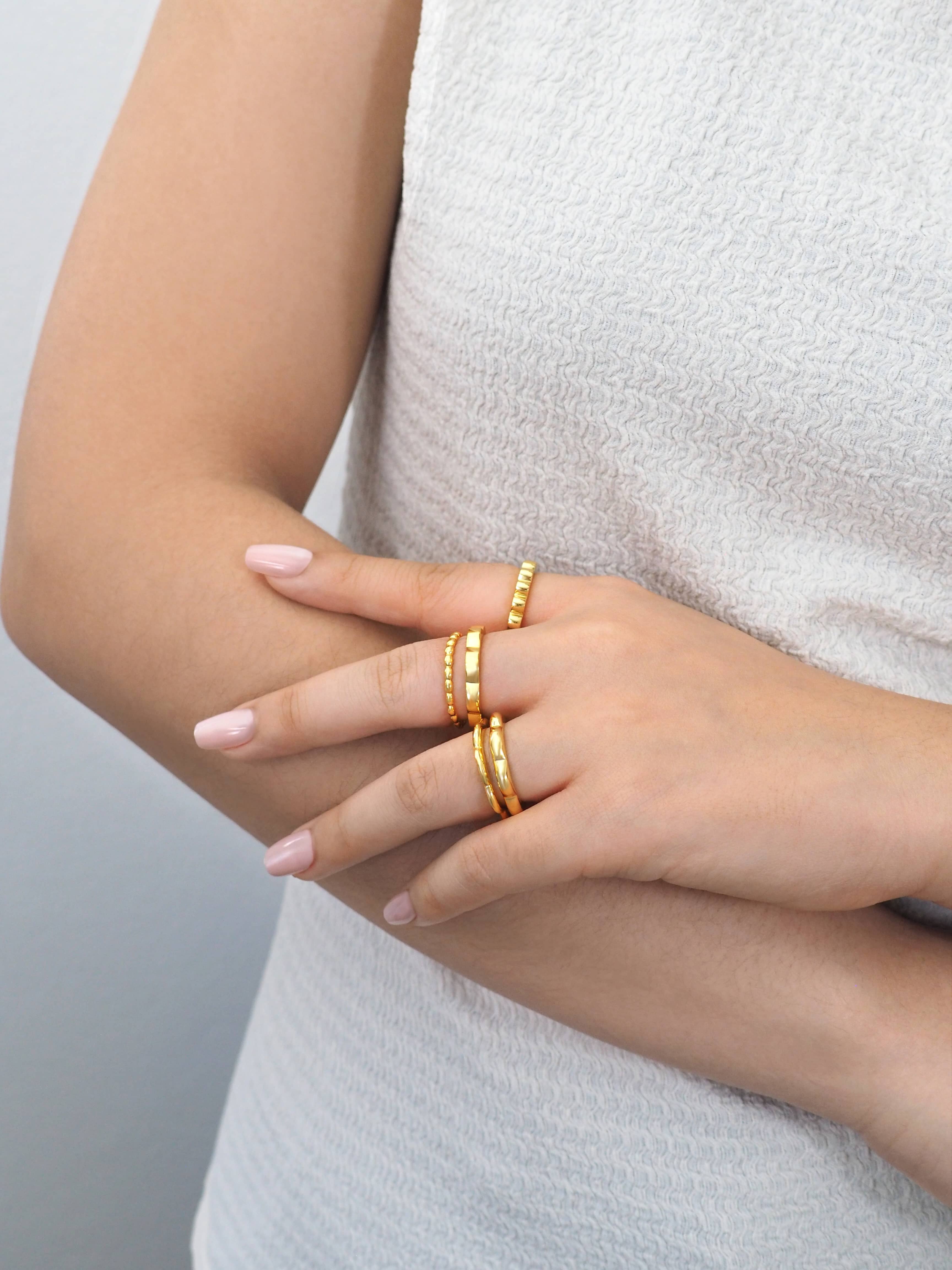Model wearing modern design of gold-plated stacking rings on fingers in casual outfit.