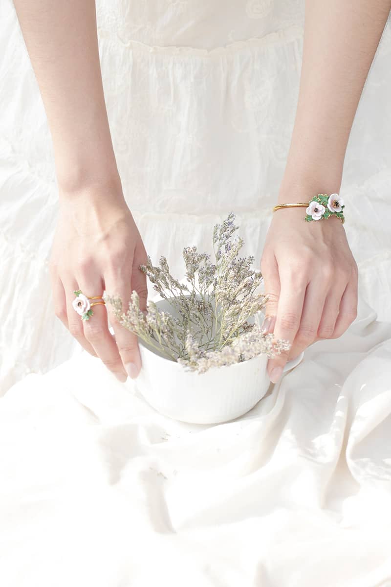 Hands showcasing a flower ring and a flower bangle while holding a bowl of flowers.