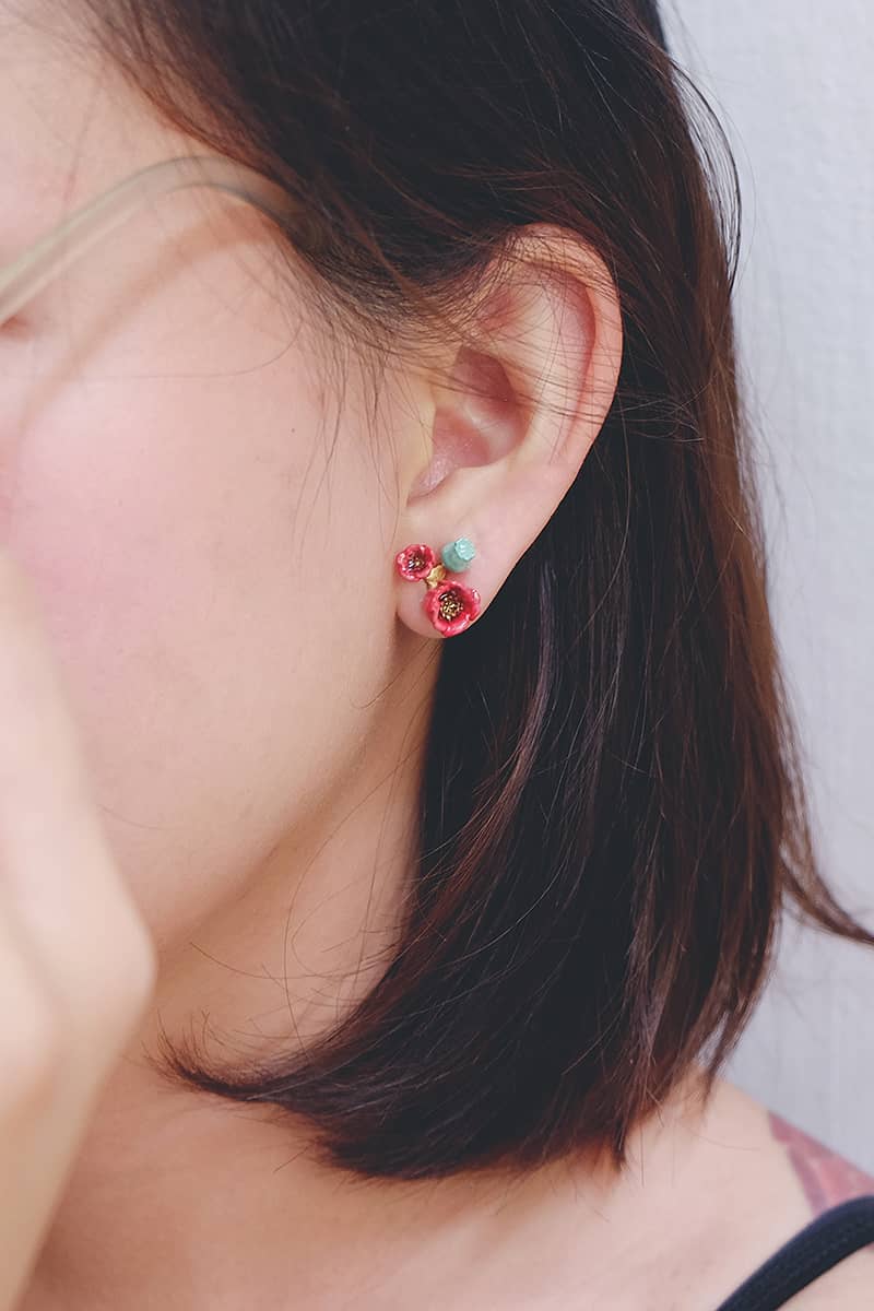 Close-up of a red floral earring with delicate poppy design worn on. a person's ear.
