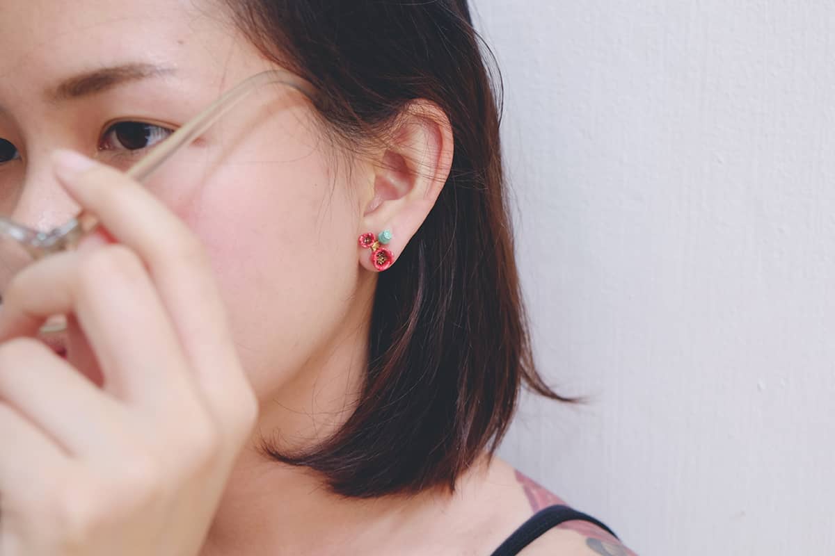 Close-up of a red floral earring with delicate poppy design worn on. a person's ear, in summer outfit.