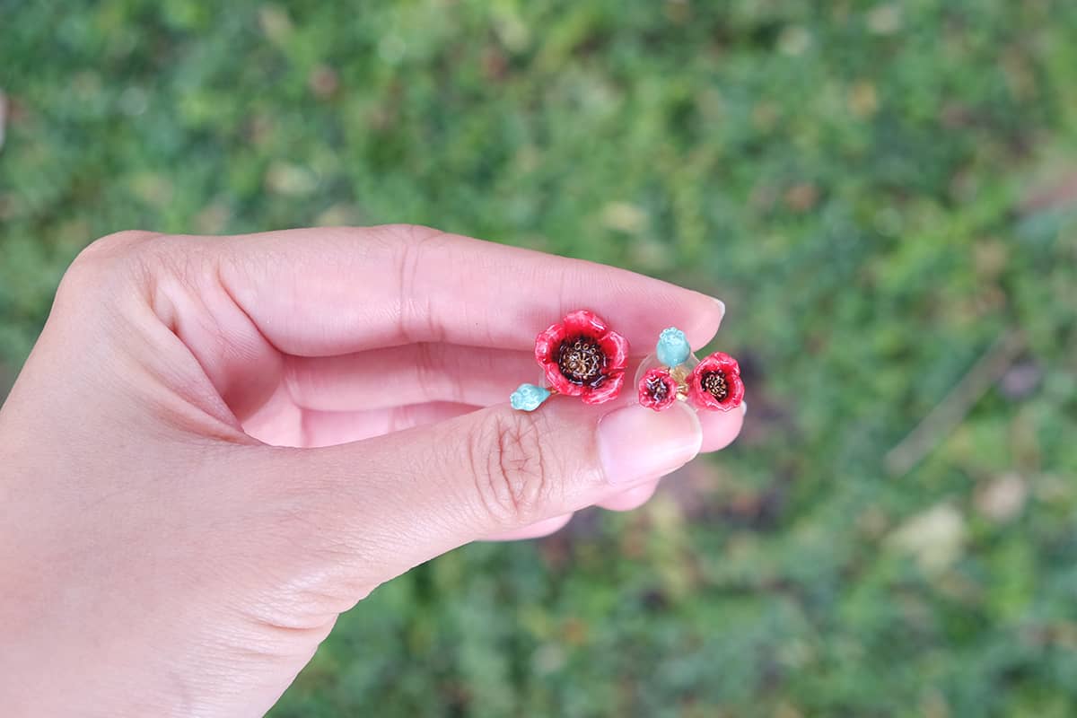 Close-up of a hand holding a red floral earring with delicate poppy design.