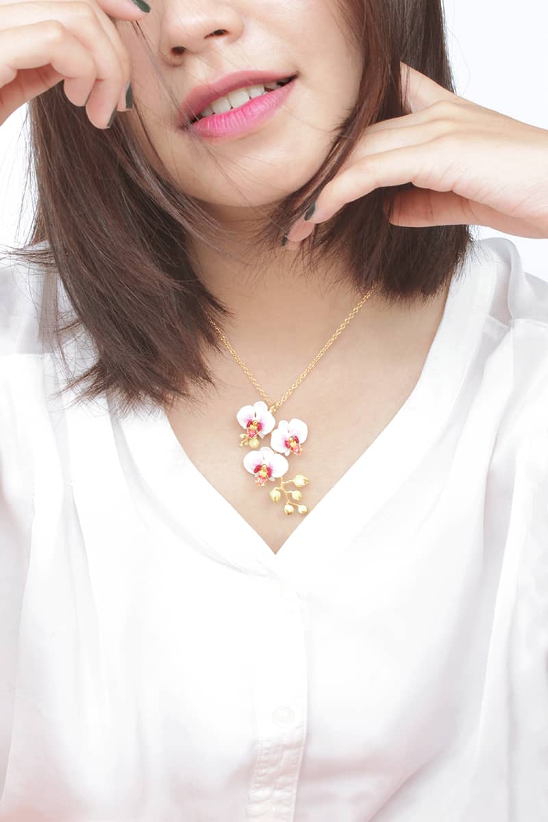 Woman wearing a white phalaen pendent necklace and a white shirt.