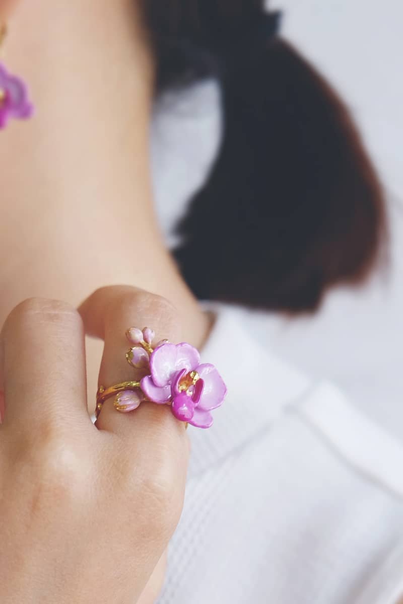Close up of a hand wearing a floral ring feating a purple phalaen design with intricate details.