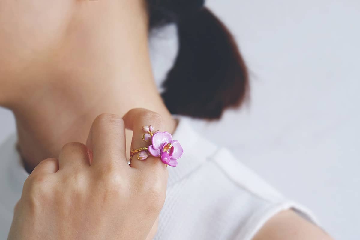 Close up of a hand wearing a floral ring feating a purple phalaen design with intricate details, ideal for summer fashion.