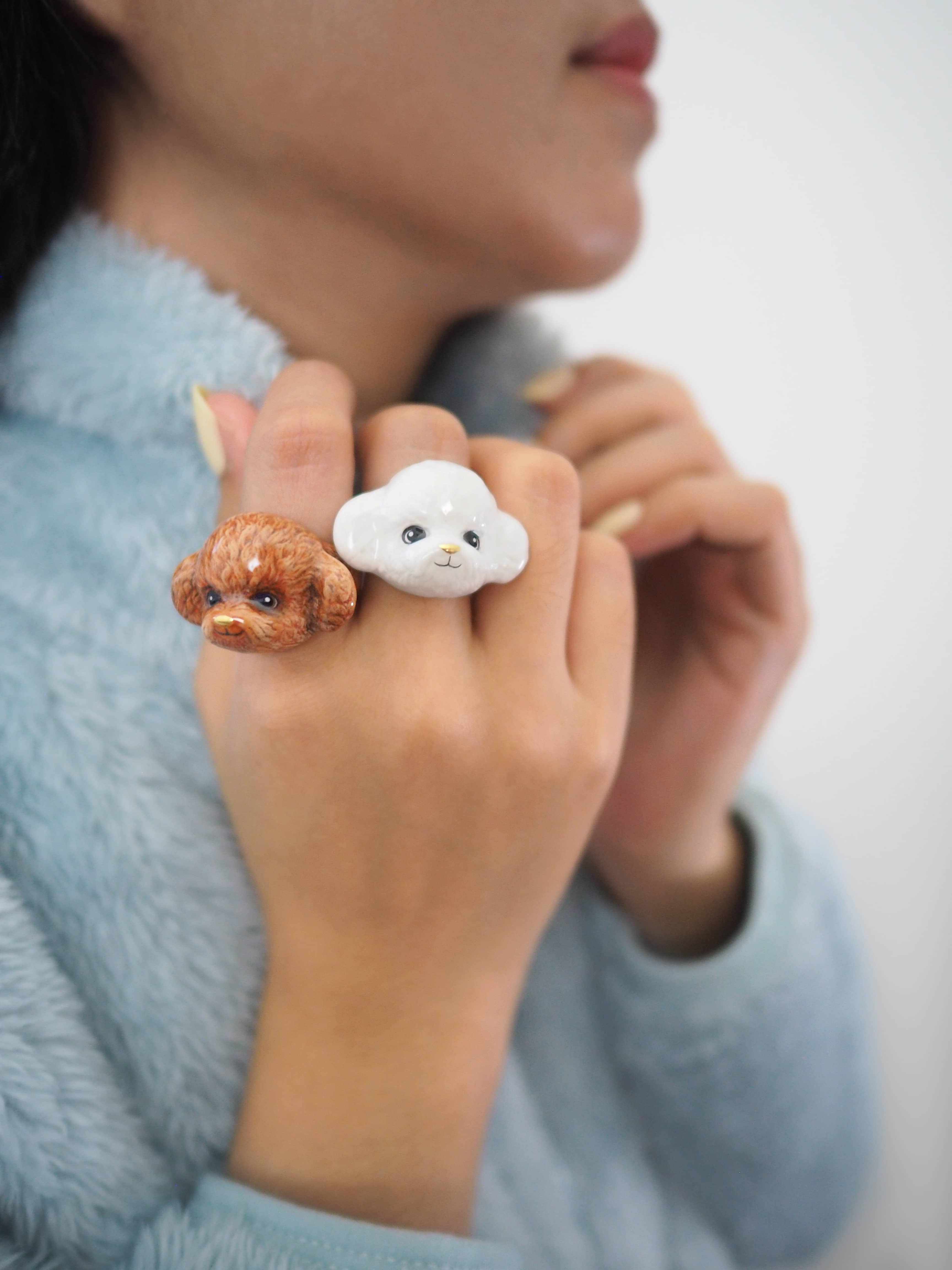 Two cute poodle rings, one brown and one white, on a person's fingers.