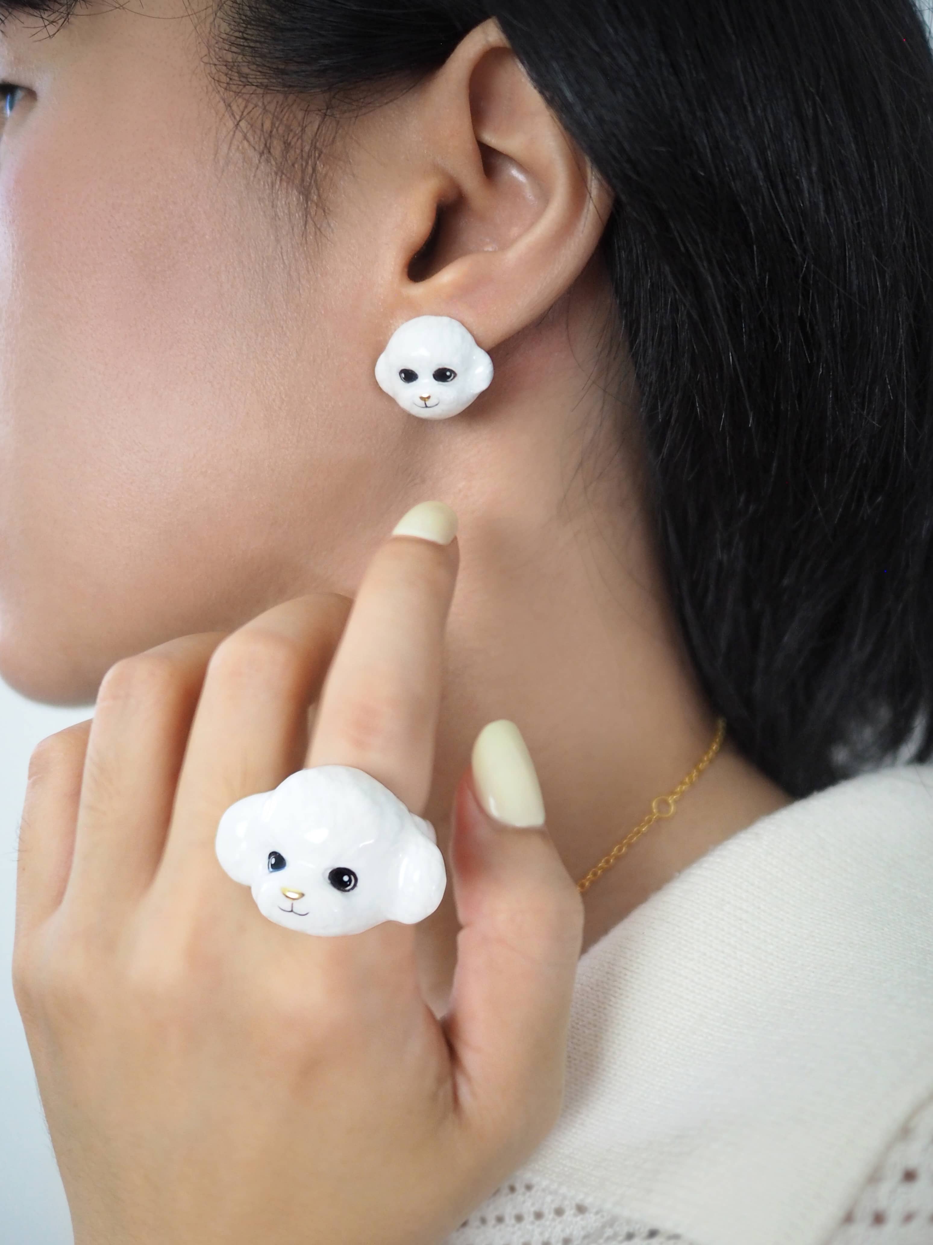 Hand-painted white poodle ring and earrings displayed on a model's hand and ear.