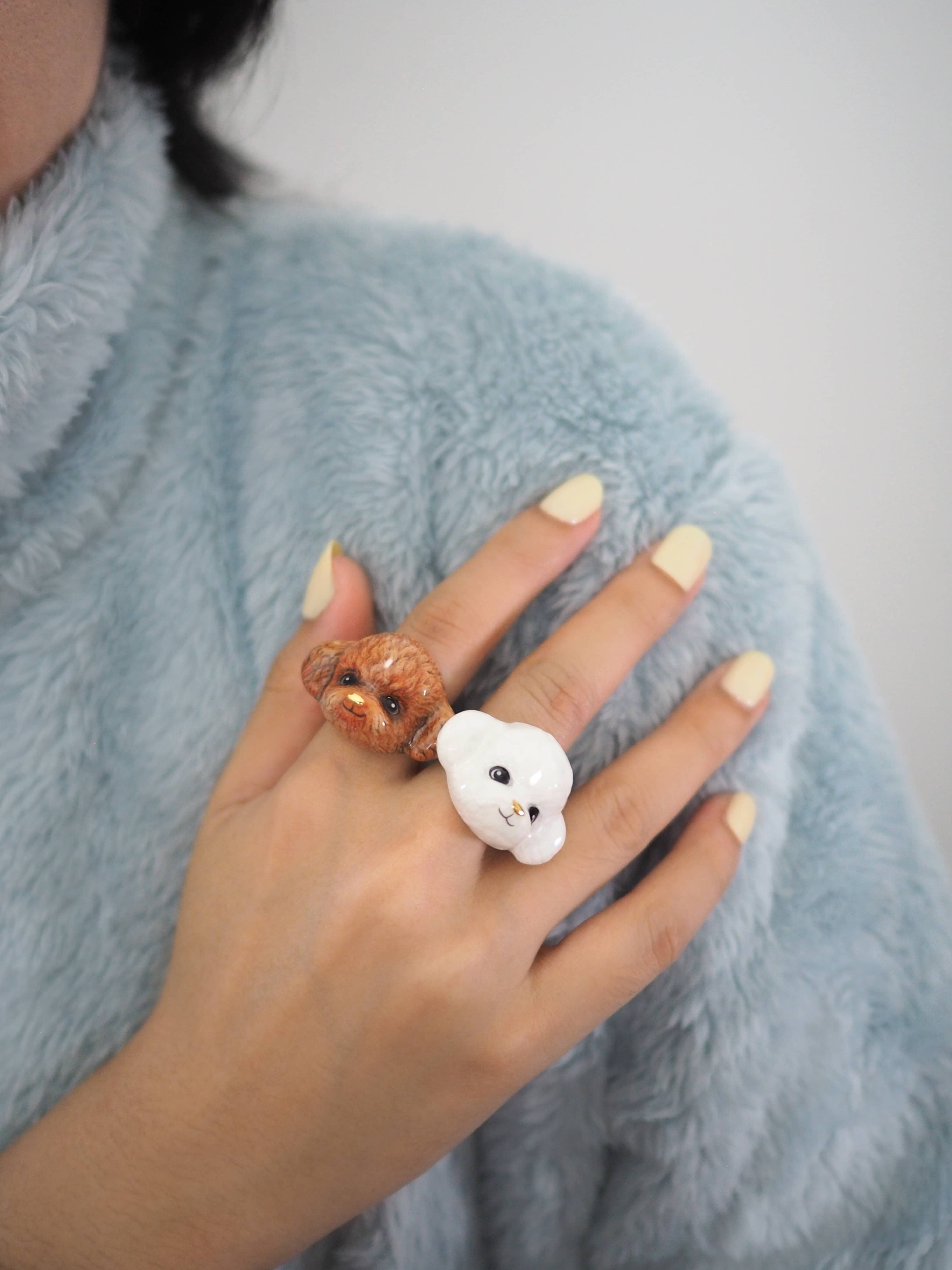 Two charming poodle rings showcasing a white and brown poodle, worn on model's fingers.