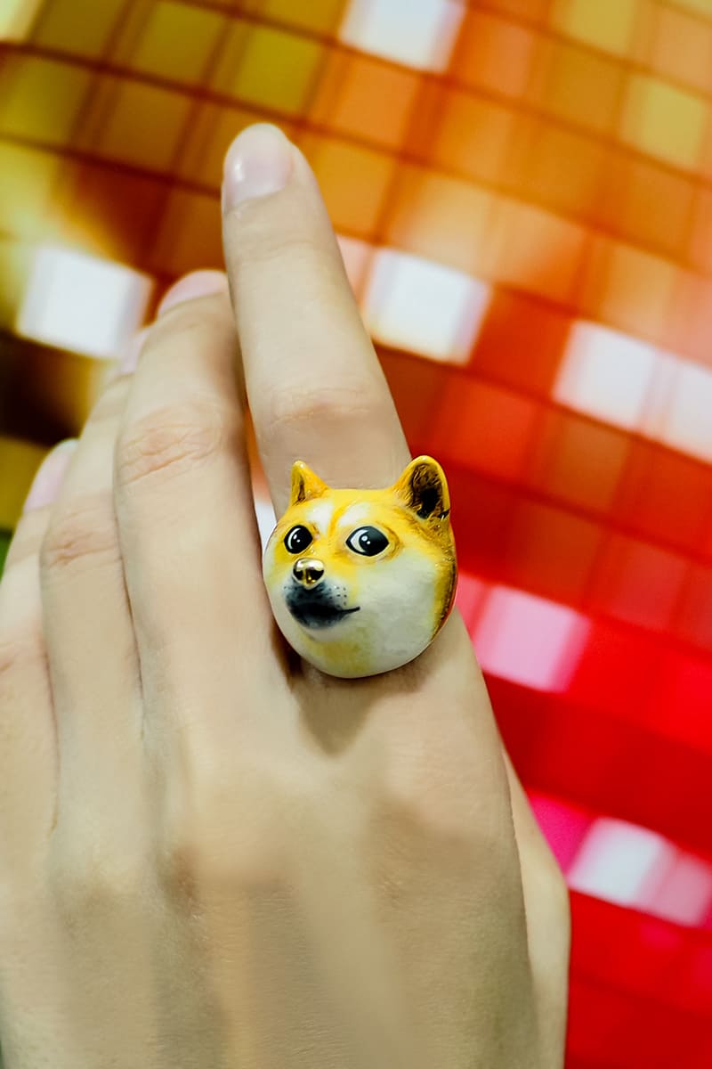 Hand wearing a doge face ring with a colorful background.