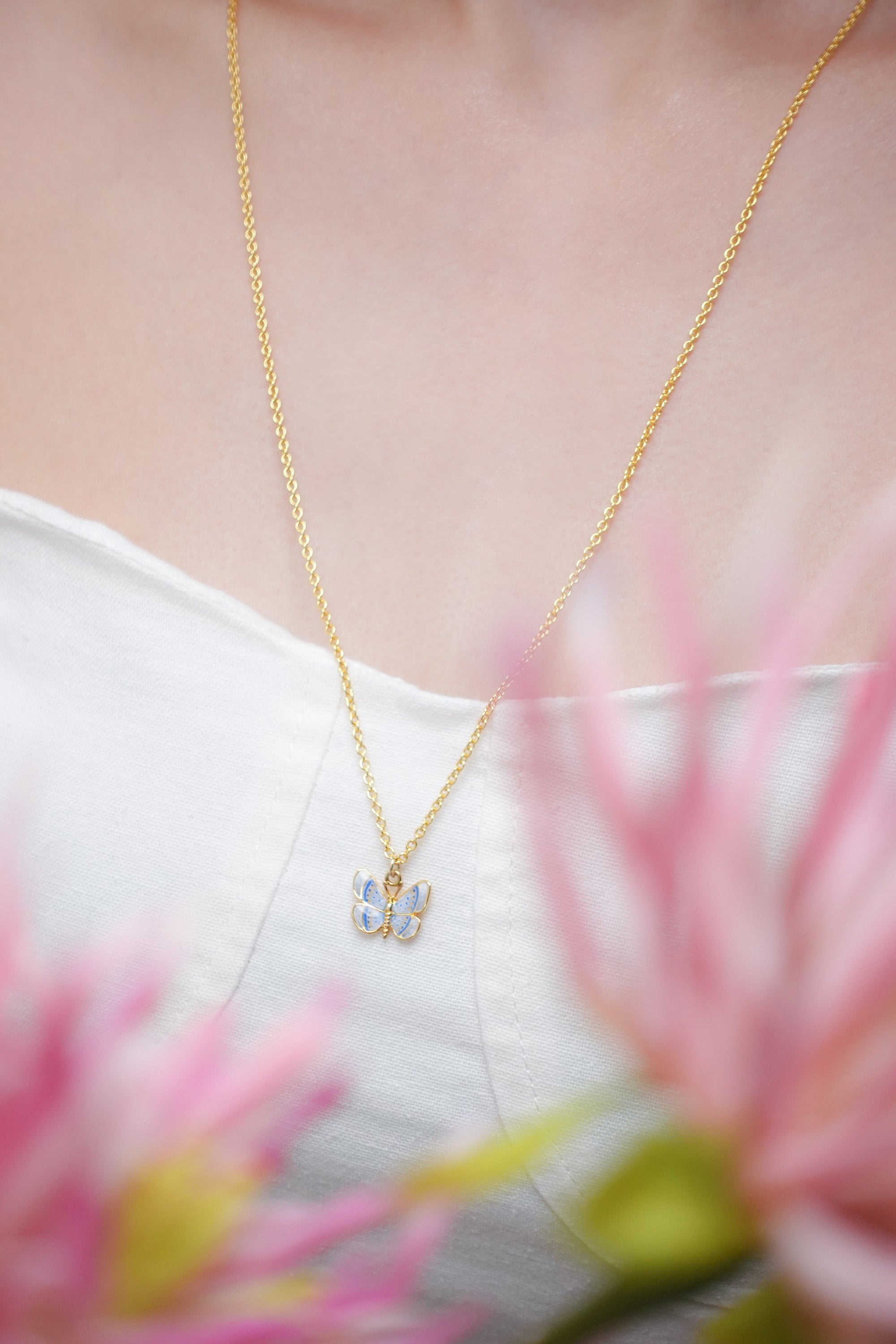 A close-up of a beautiful gold necklace with a butterfly pendant, surrounded by pink flowers.