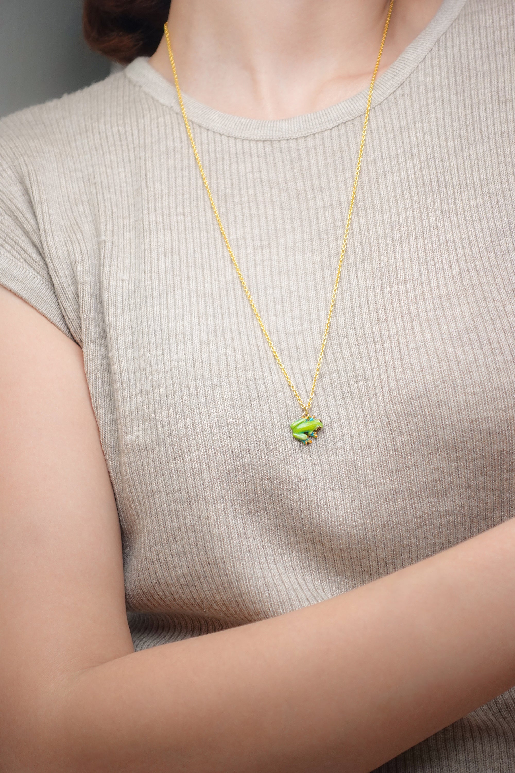 Close-up of a model wearing a frog pendant necklace on a gold chain.