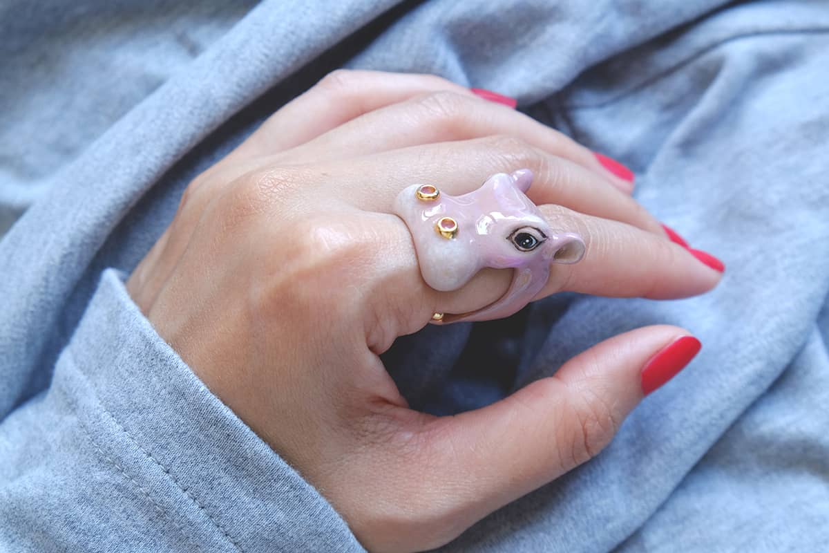 A cute hippo ring worn on a hand with red nails.