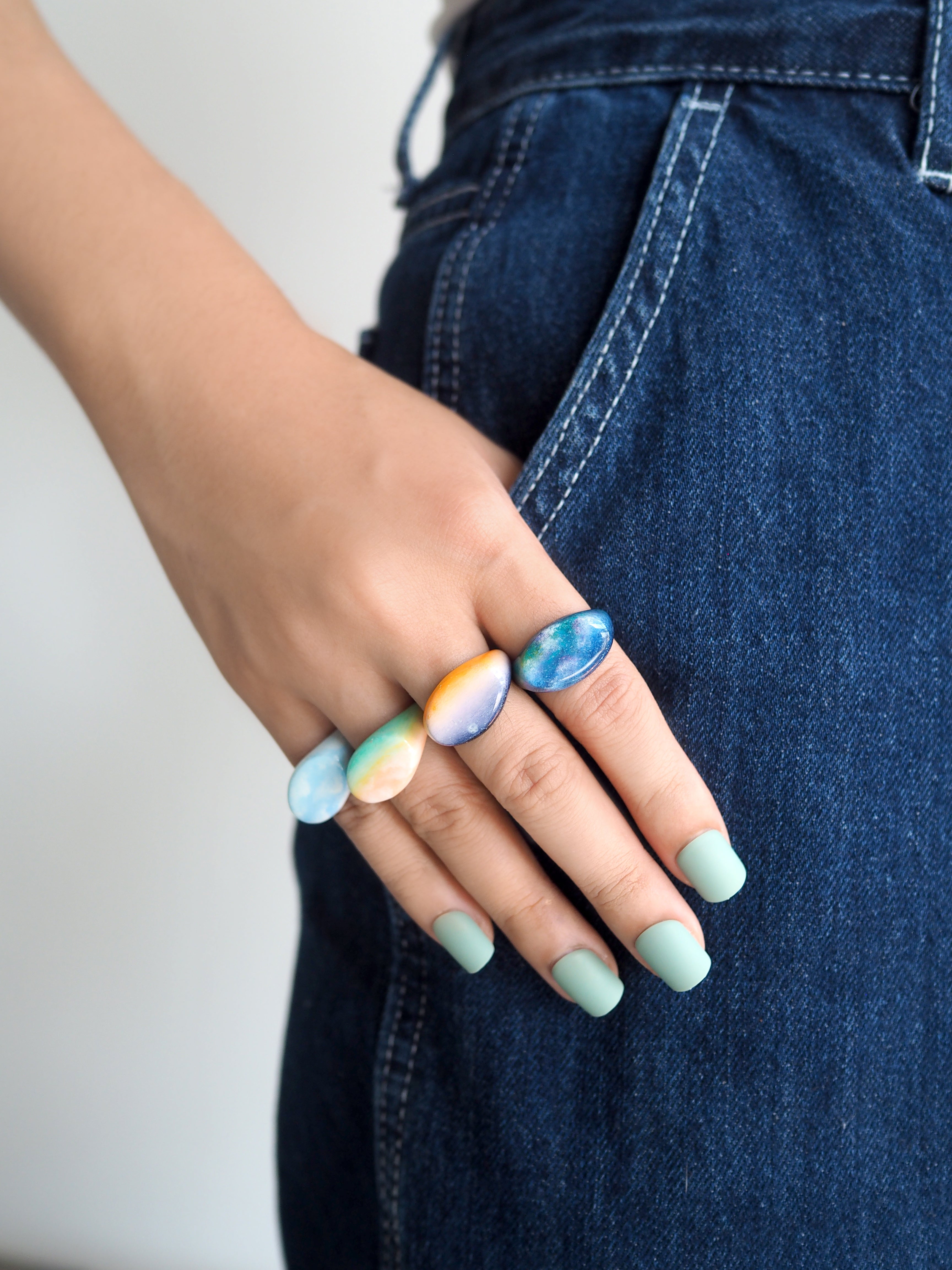 Unique hand-painted rings showcasing sky colors worn on a hand.