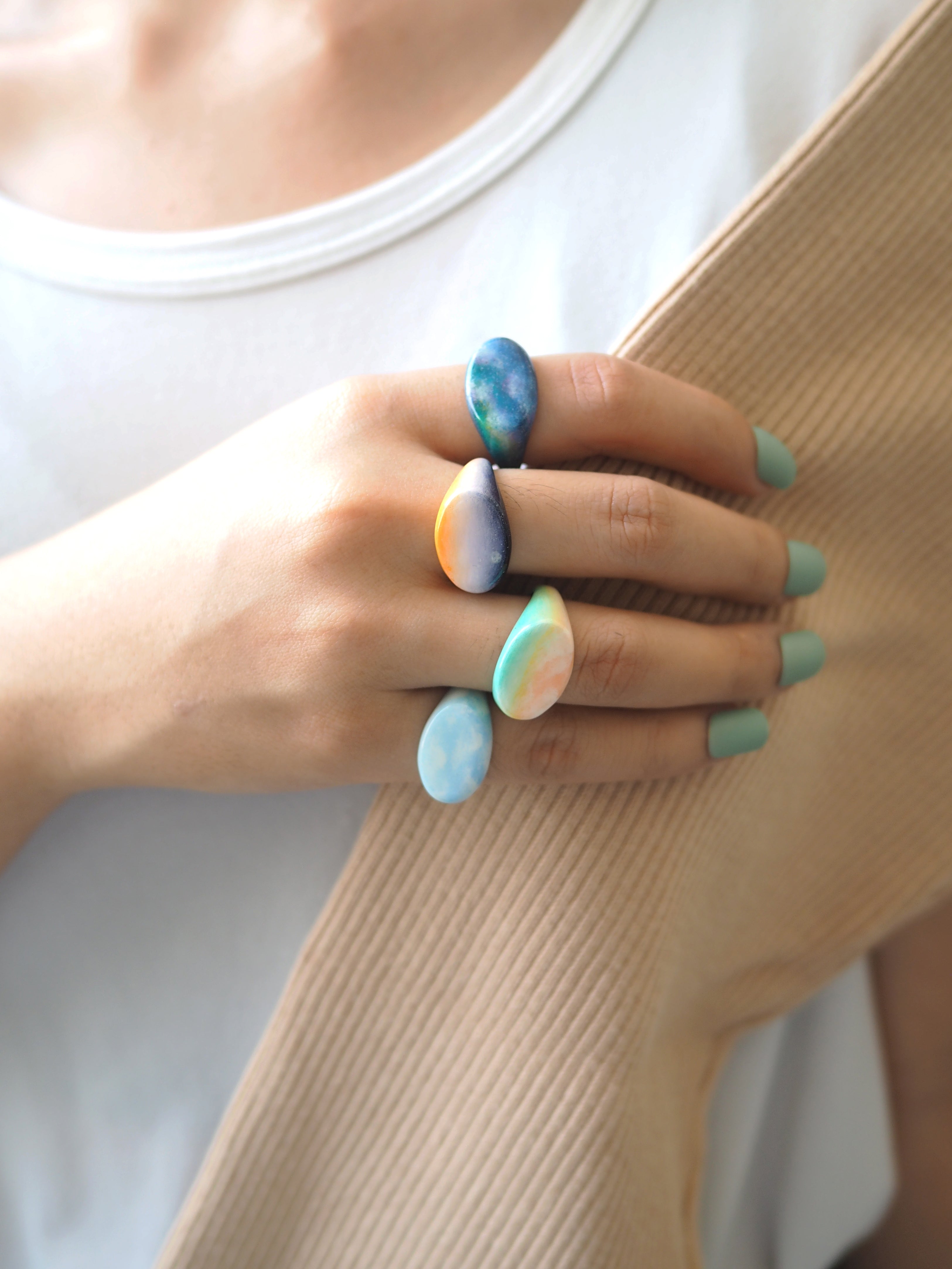 Hand-painted rings in shades of sky colors on a woman's hand.