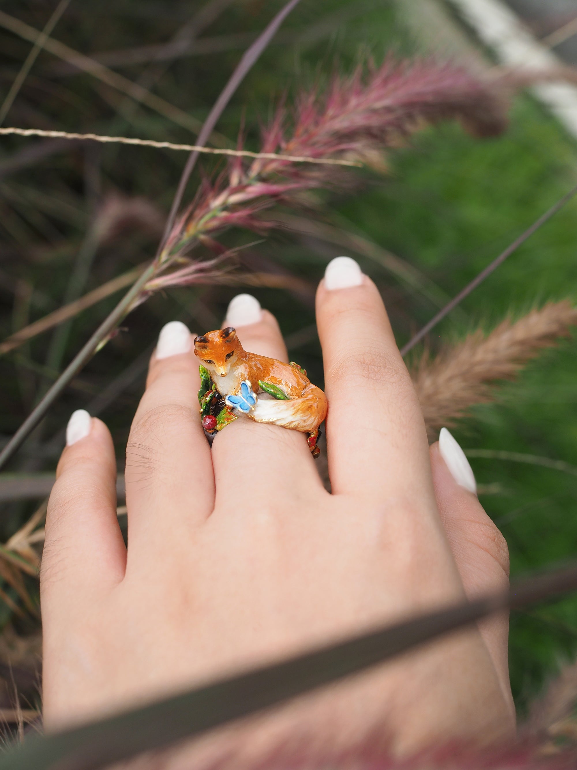 Artistic ring featuring a fox and decorative elements, displayed on a hand in a natural setting.