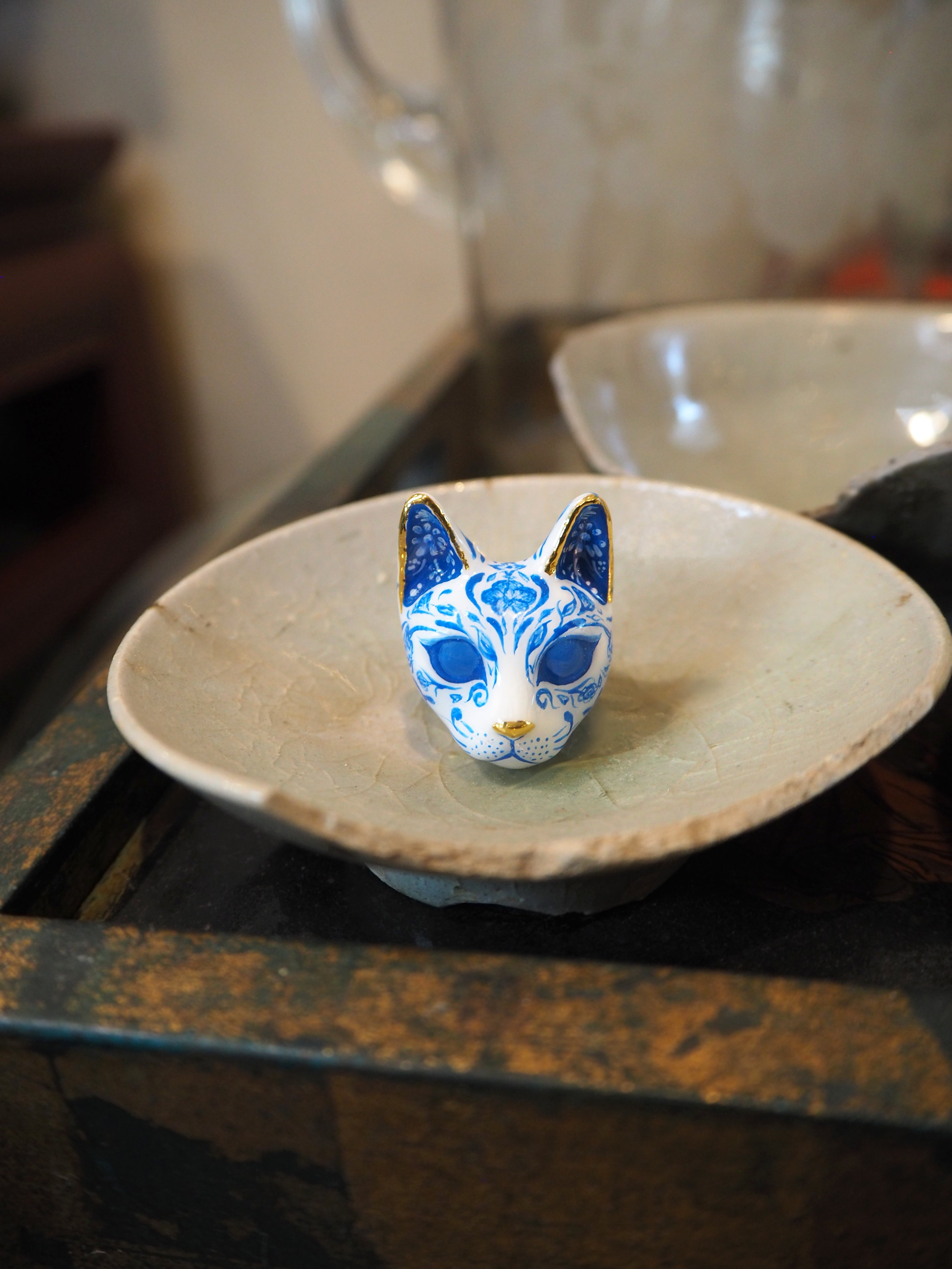 Hand-paint cat's face ring featuring detailed porcelain patterns, painted in blue and white pattern with gold accents, place on a broken plate.