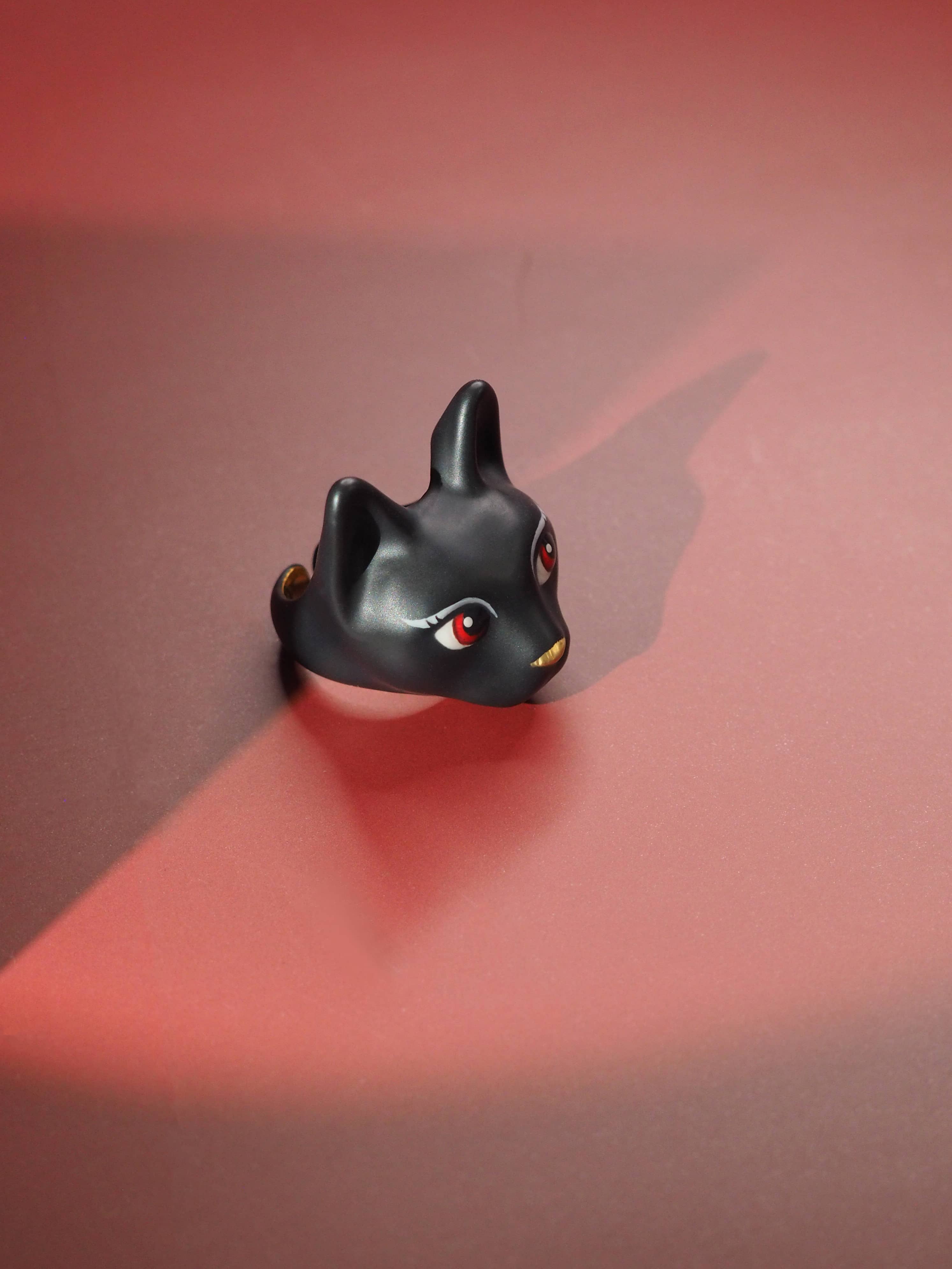 A charming hand-painted ring showcasing a black cat with fierce red eyes placed on red background.