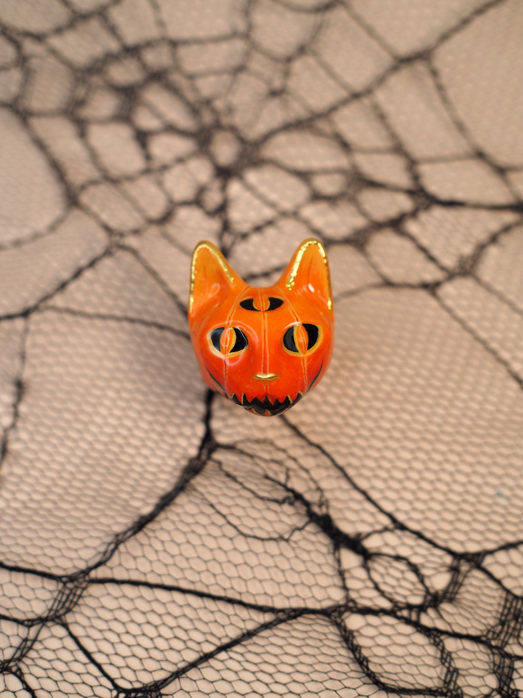 Halloween-themed ring inspired by a jack-o-lantern with cat features placed on a decorative spider eweb.