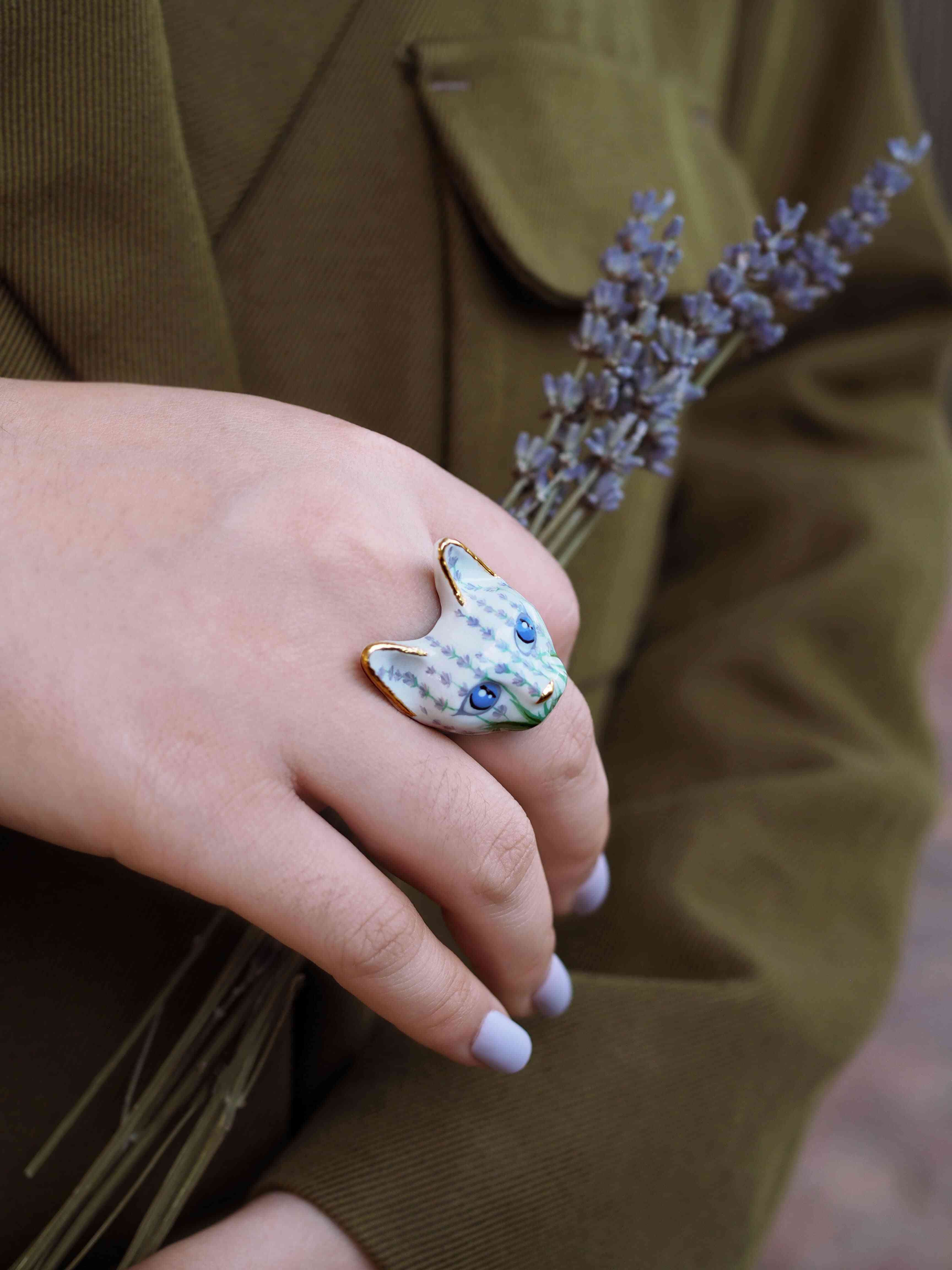 A hand adorned with a unique cat ring featuring floral pattern, holding a bundle of lavender flowers.