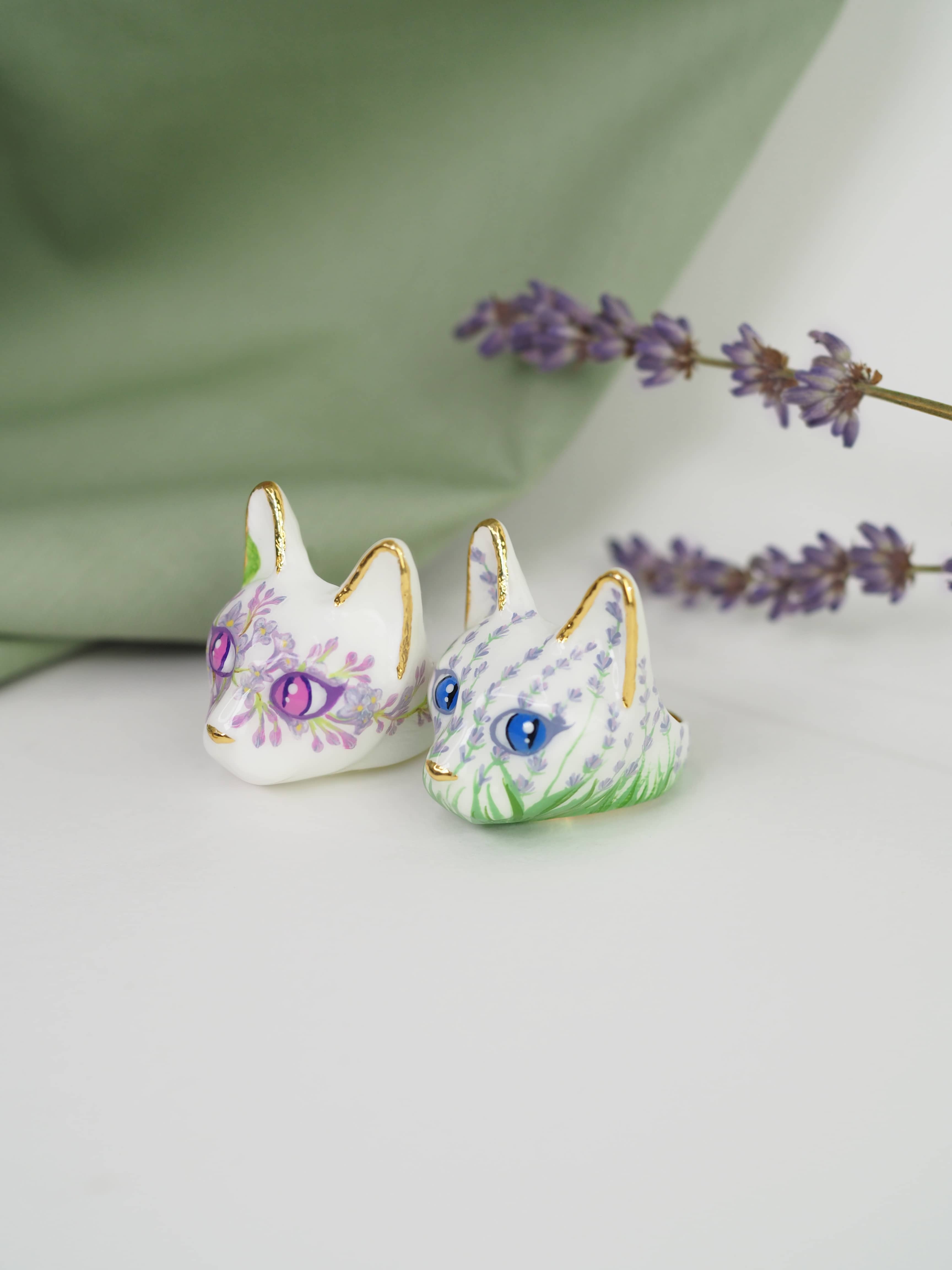 Two unique cat rings with colorful floral patterns placed against a soft green background, alongside sprigs of lavender.