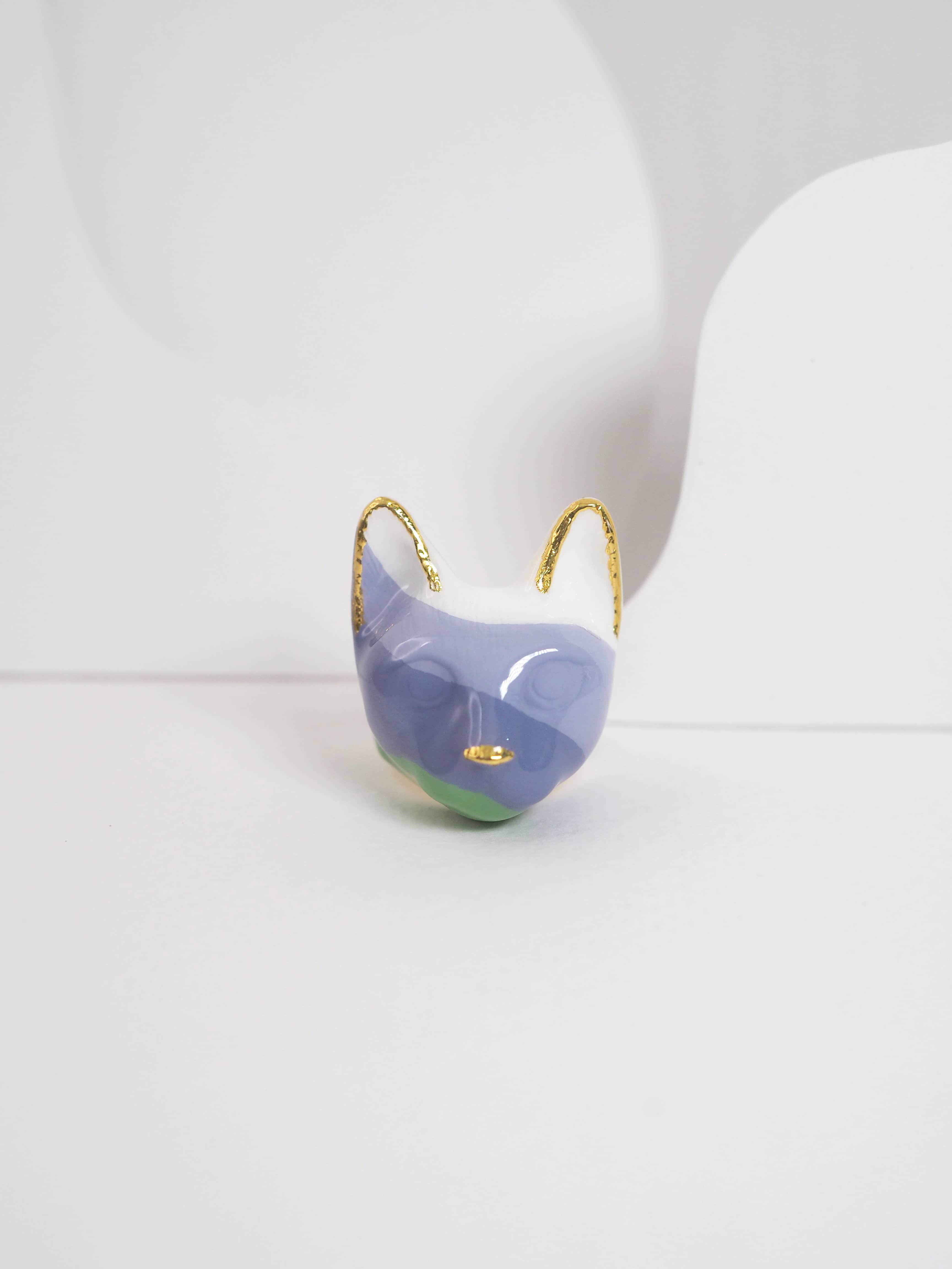 A unique cat ring in pastel colors, purple, green, and white, set against a light background.