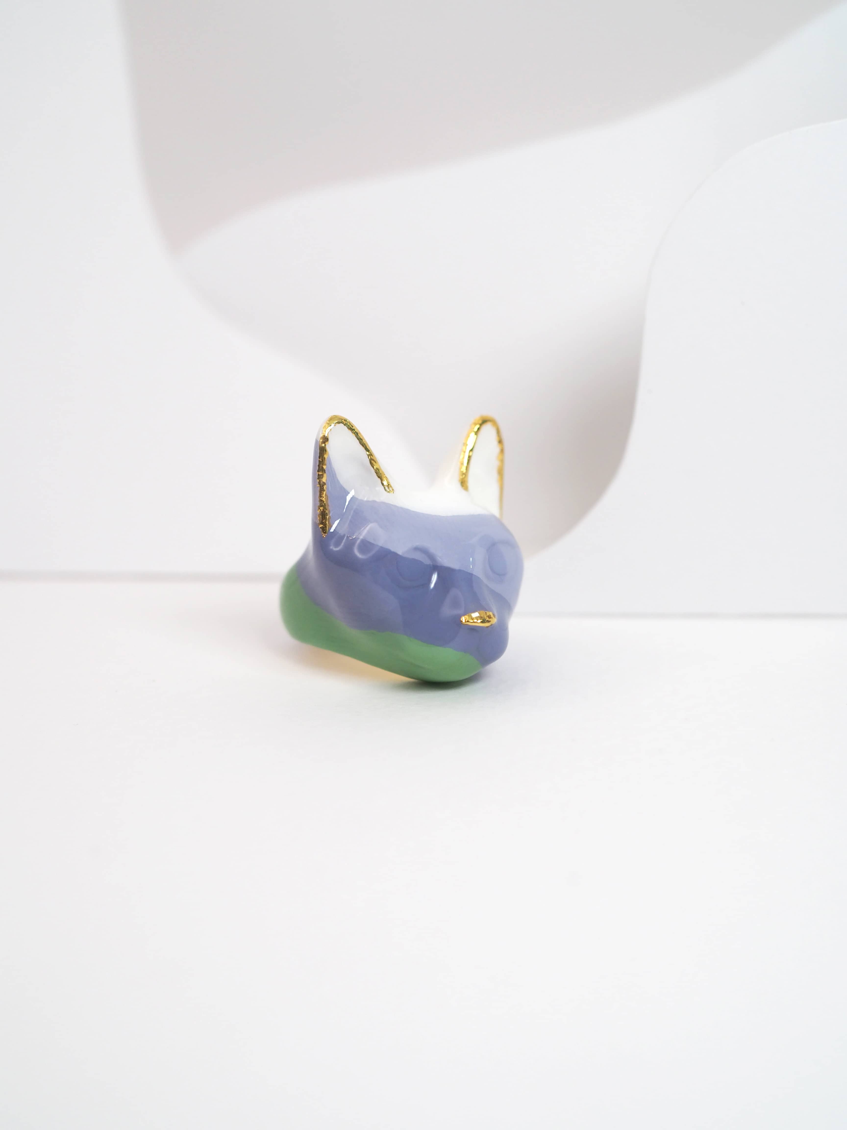 A unique cat ring in pastel colors, purple, green, and white, set against a light background.