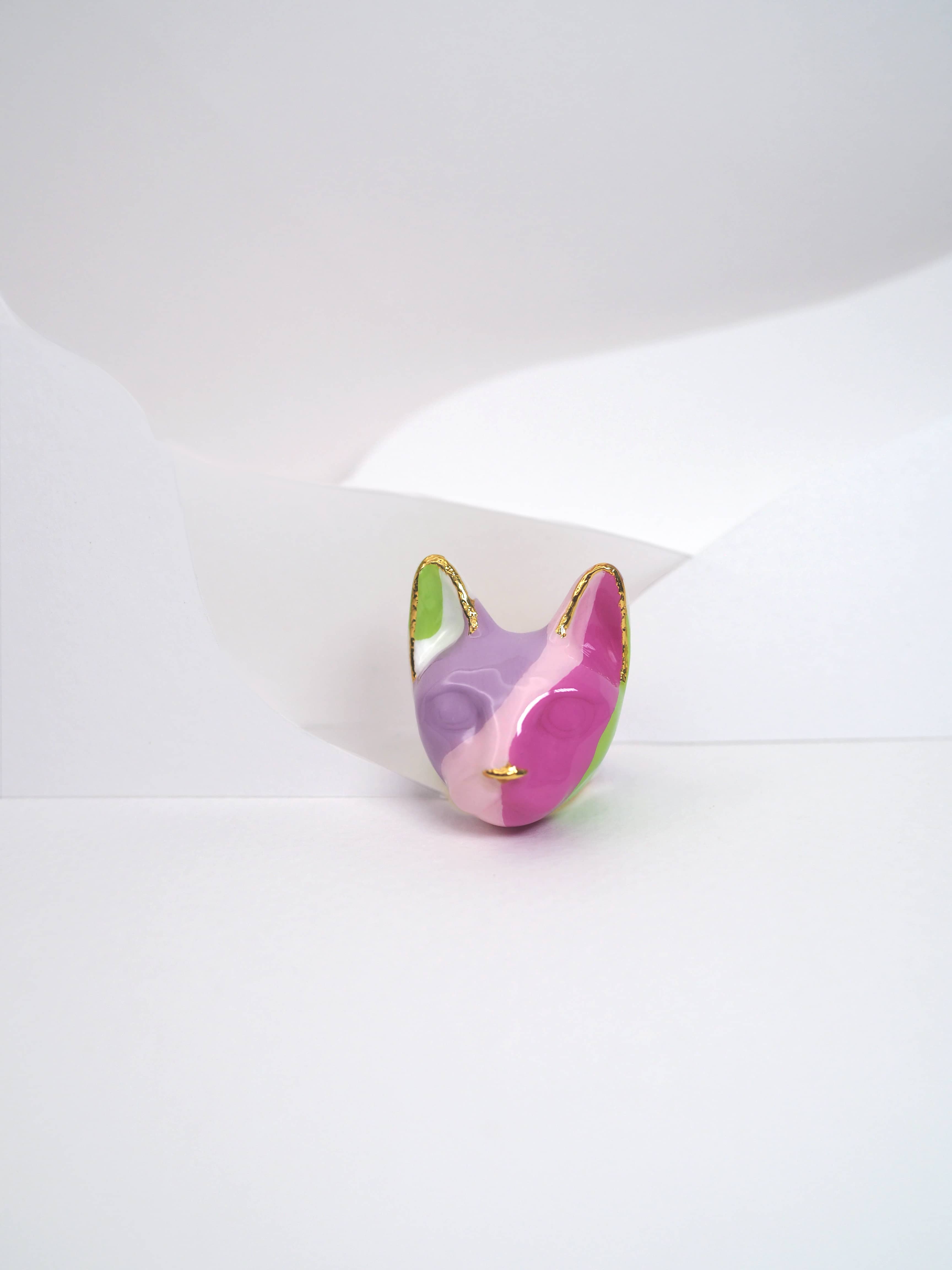 A unique pattern cat ring with geometric shapes in purple, pink, green, and white, placed in a light background.