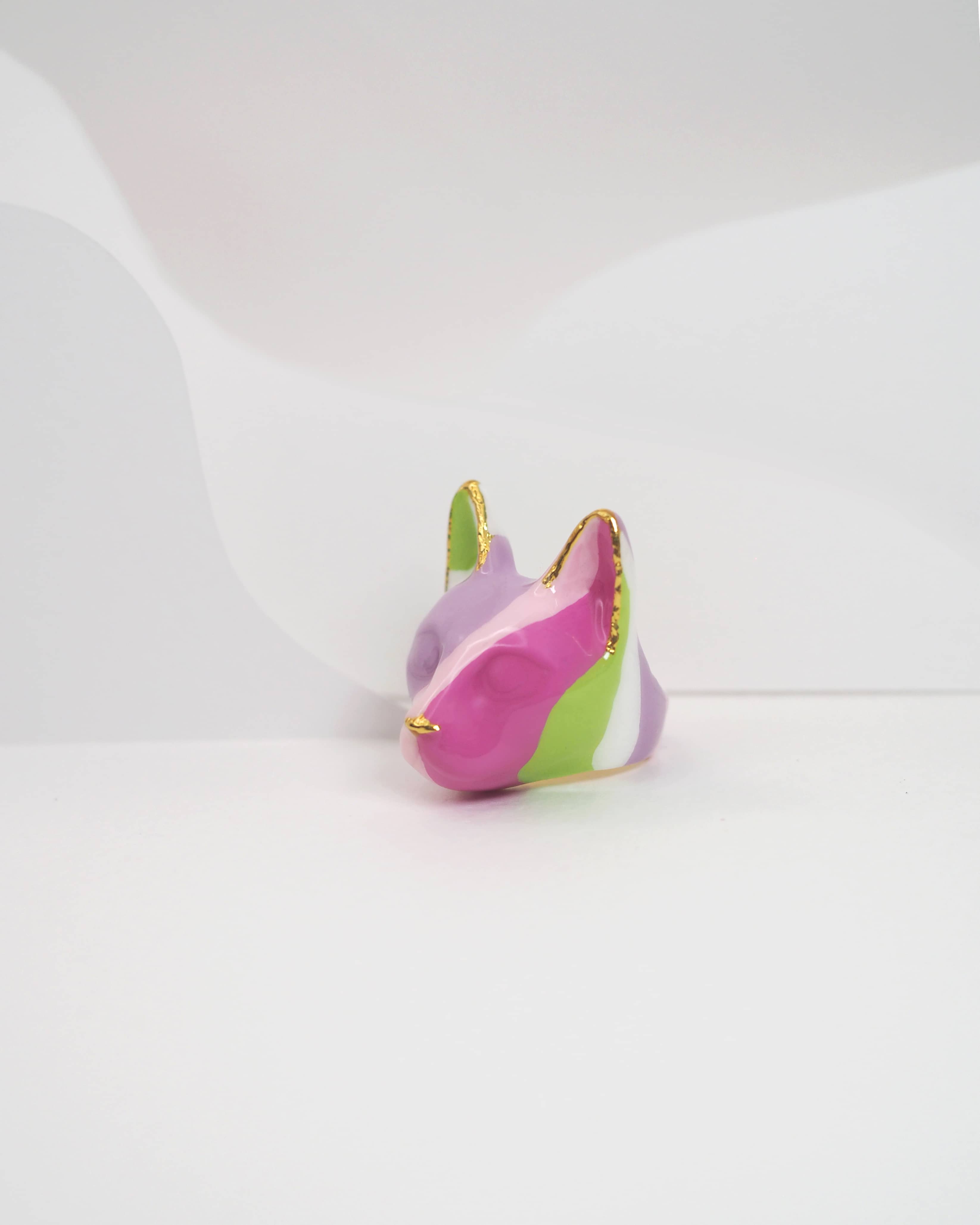 A unique pattern cat ring with geometric shapes in purple, pink, green, and white, placed in a light background.