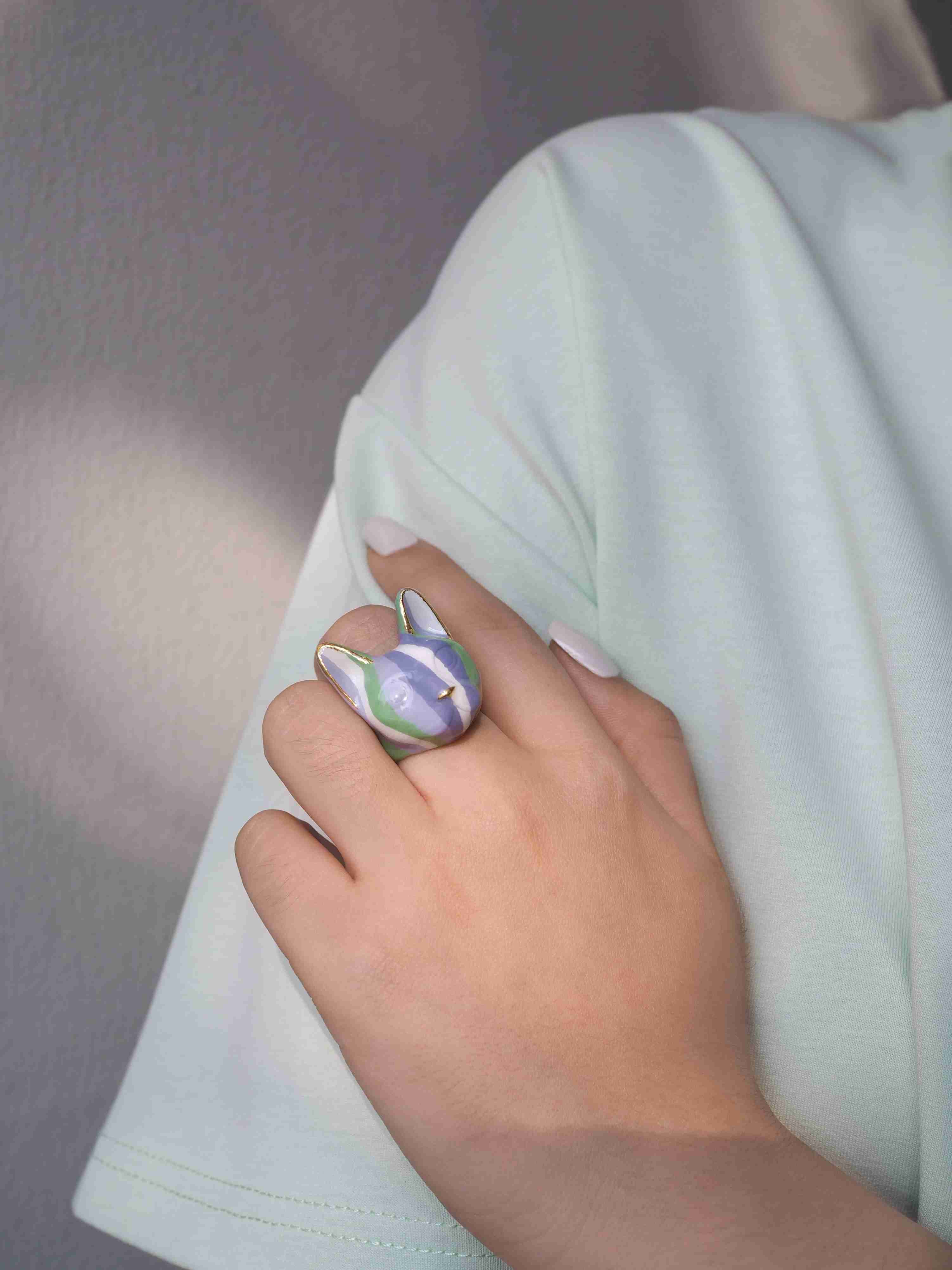 Close-up of a hand wearing a cat ring designed with stripes of green and purple.