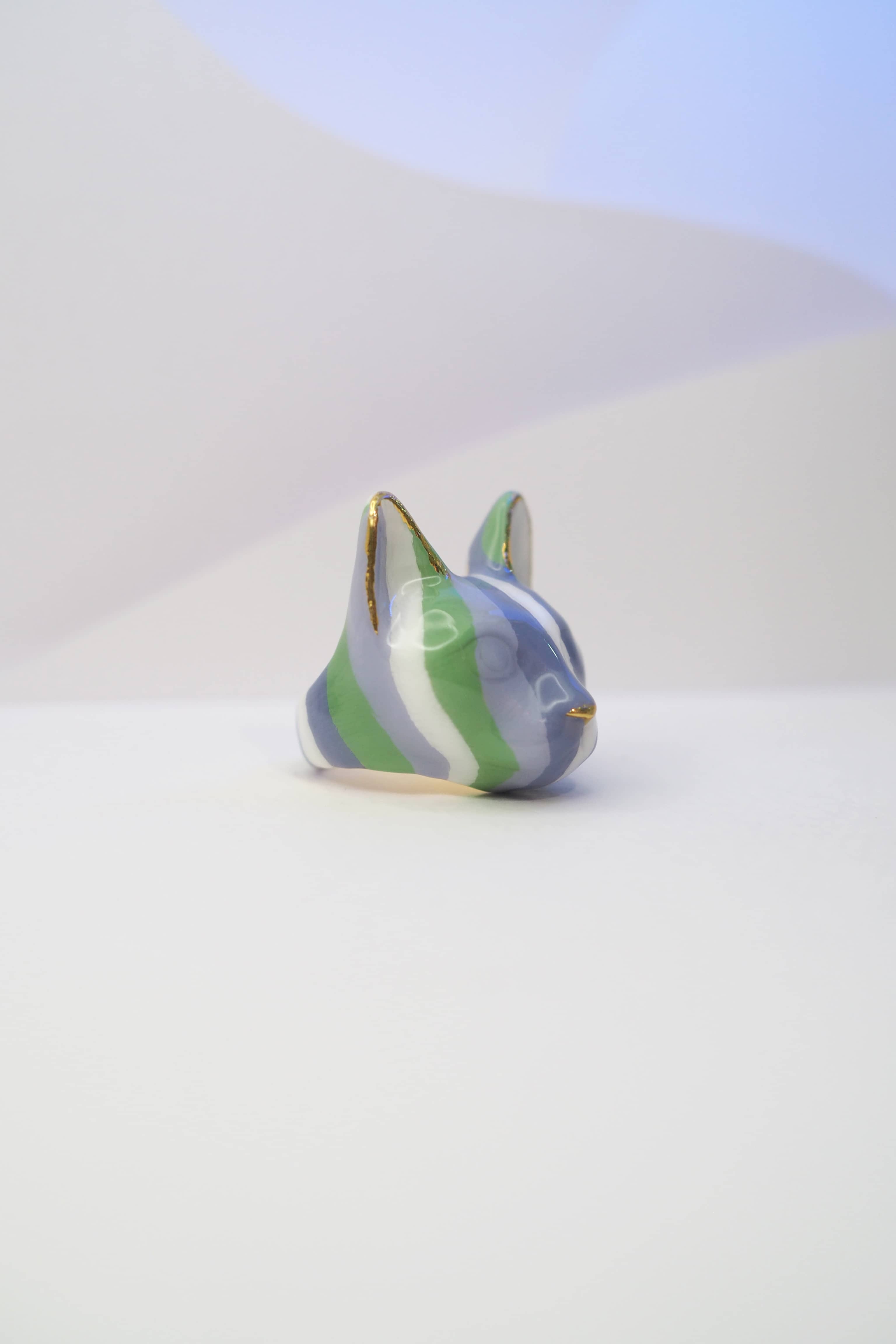 Close-up of a cat ring designed with stripes of green and purple placed on a white background.