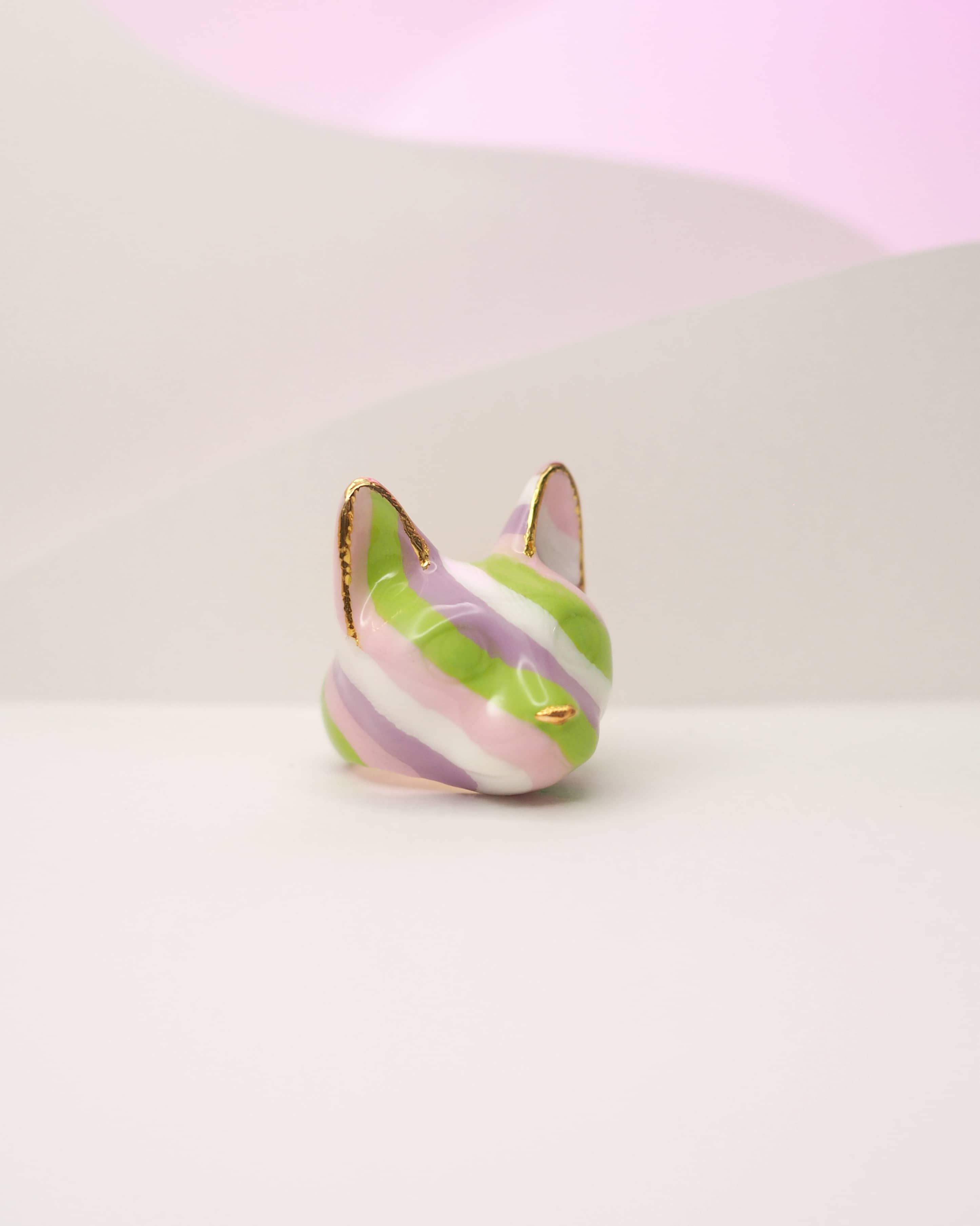 Close-up of a cat ring designed with stripes of green, purple, and pink placed on a white background.