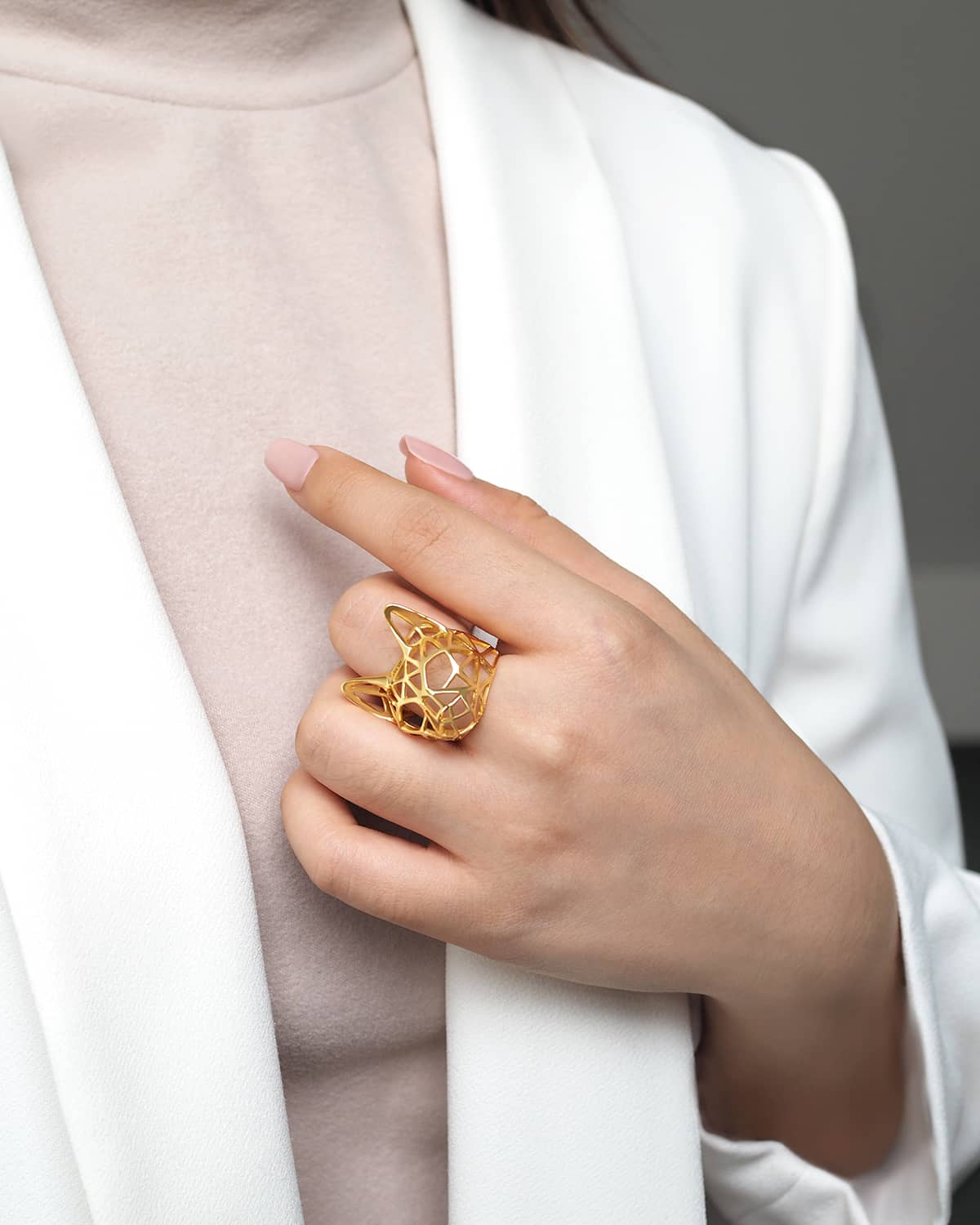 A hand wearing a unique cat-shaped ring with a modern design in gold.
