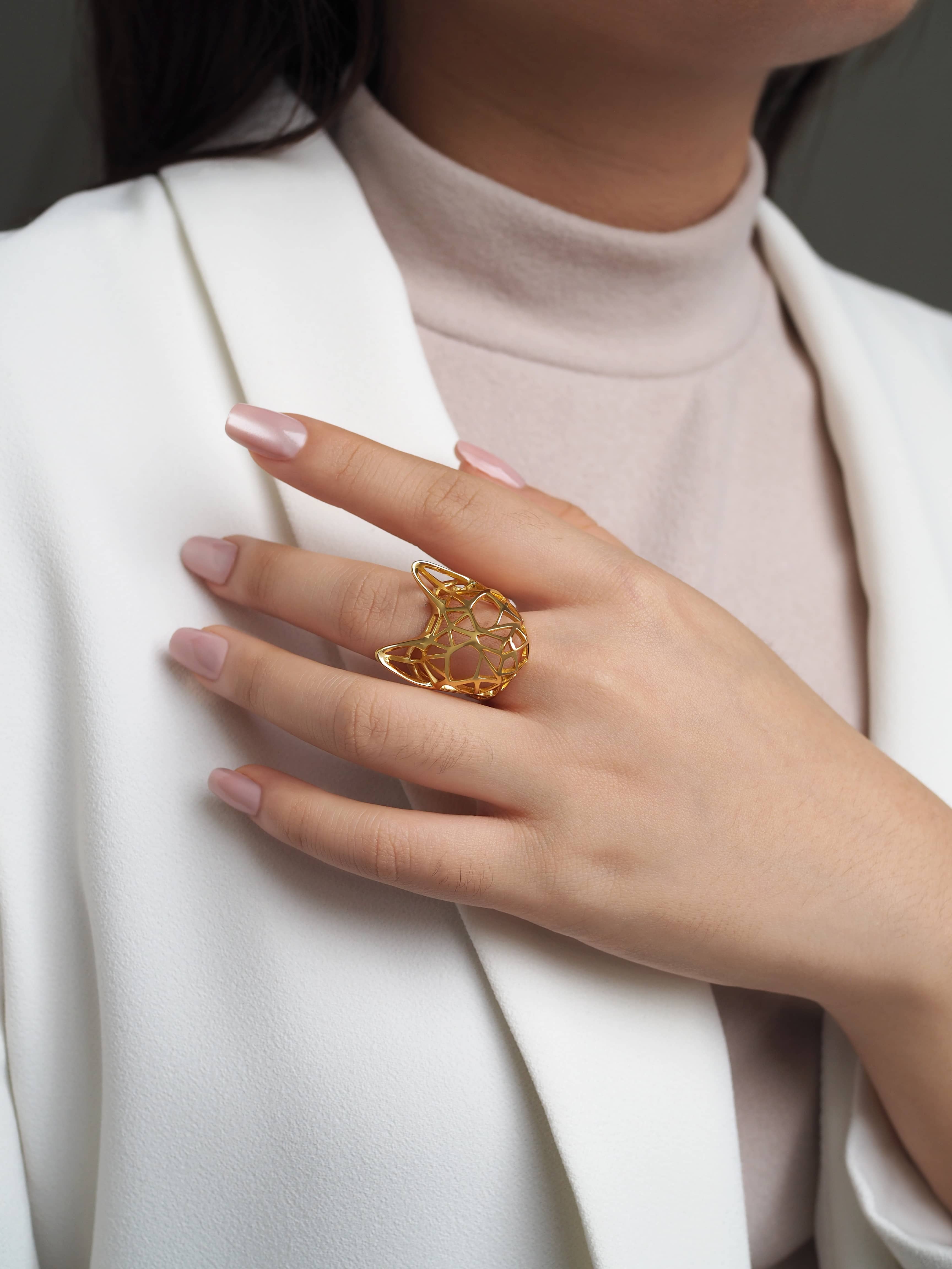 A hand wearing a unique cat-shaped ring with a modern design in gold.