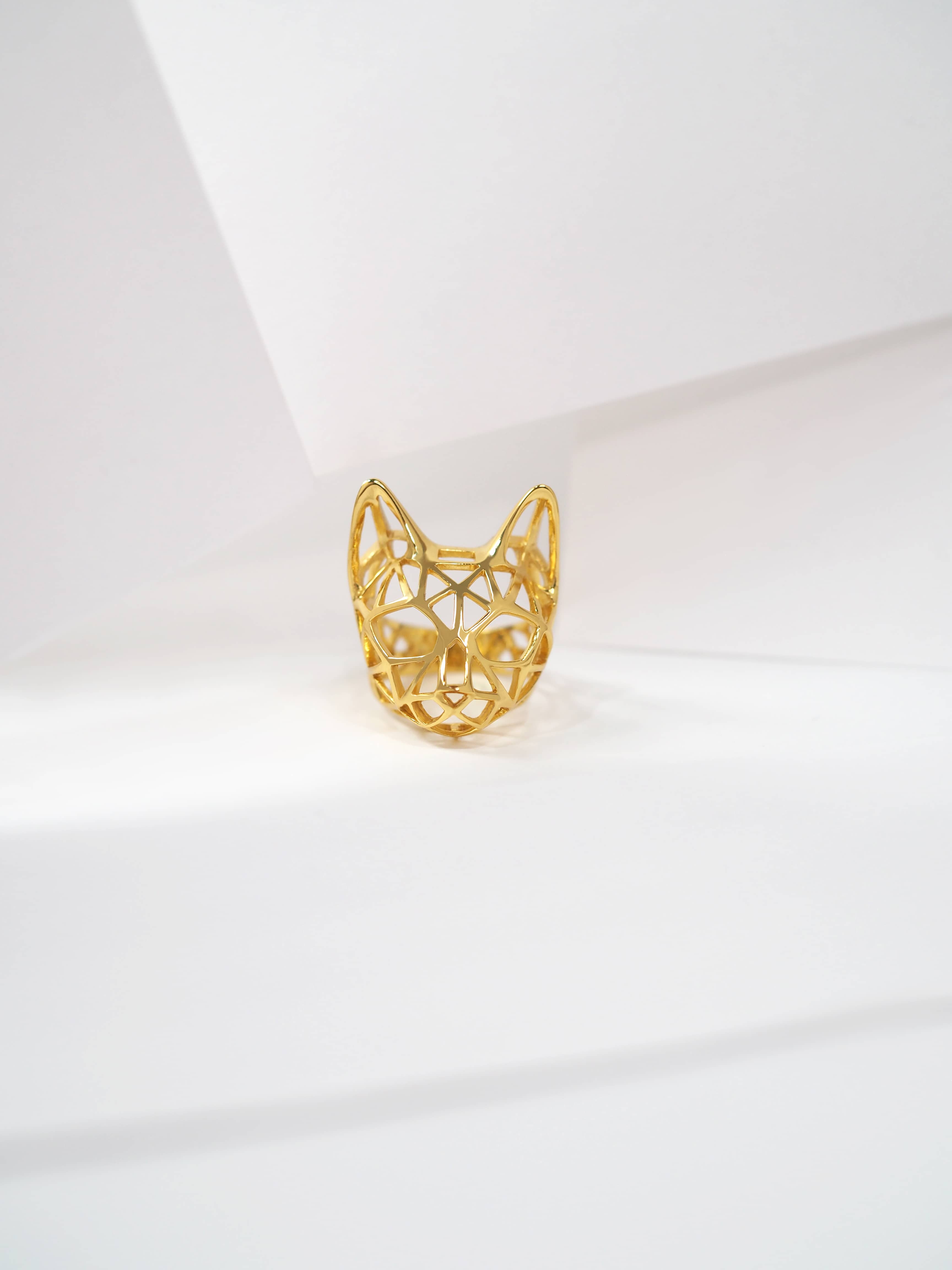 Artistic golden ring featuring a cat head design rest on white background.
