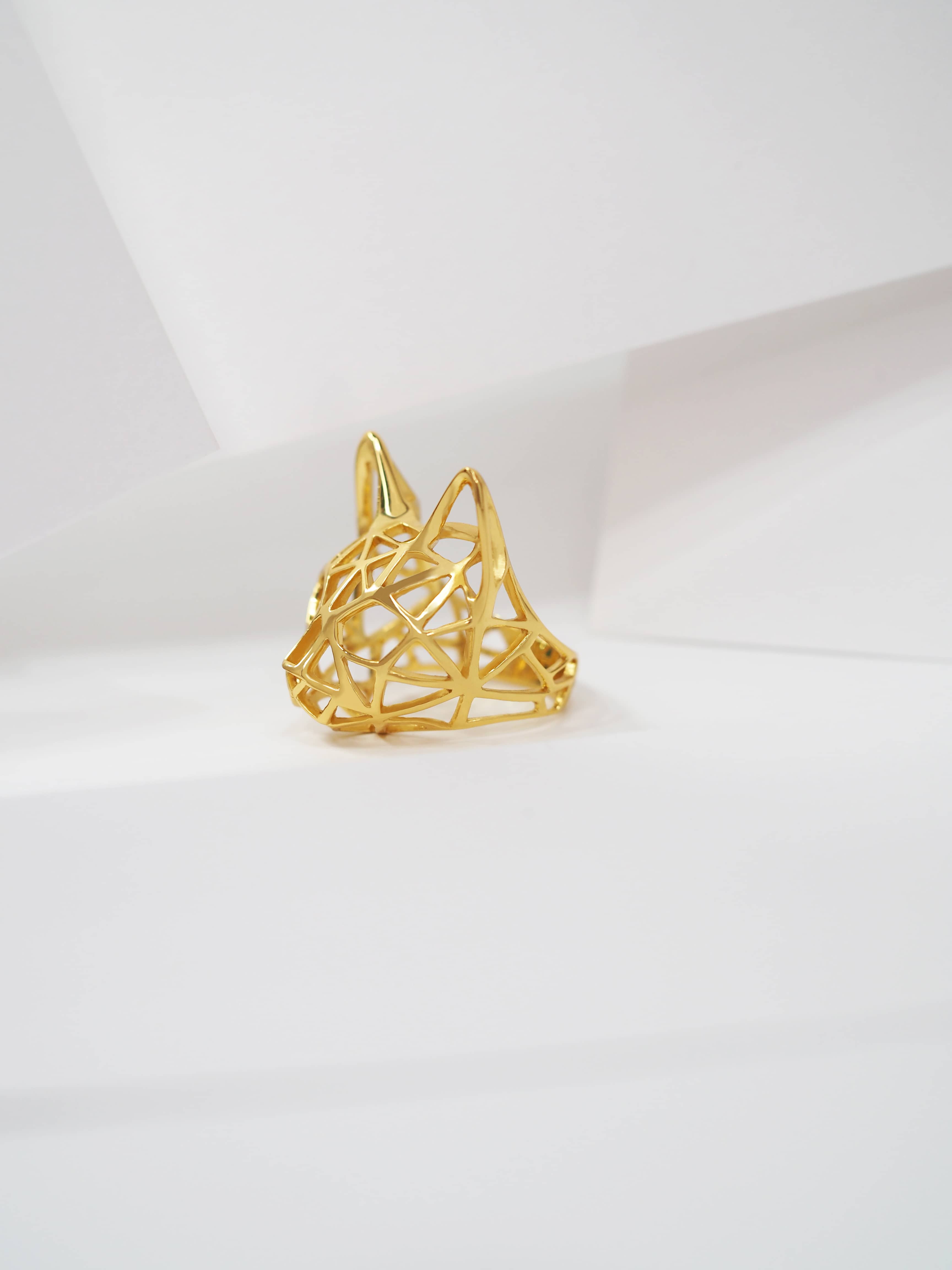 Artistic golden ring featuring a cat head design rest on white background.