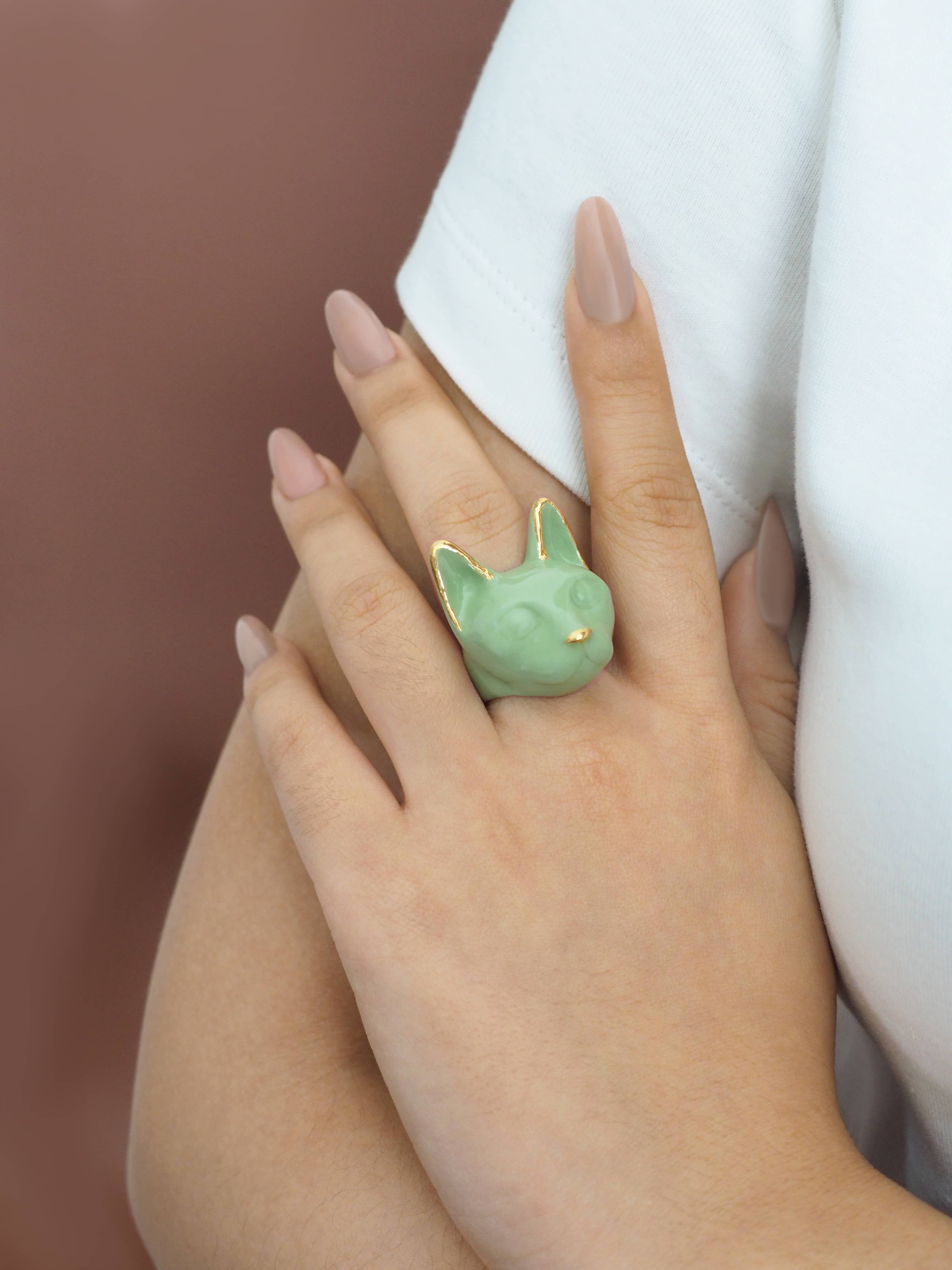 Unique cat face jewelry, showcasing a green ring on a finger.