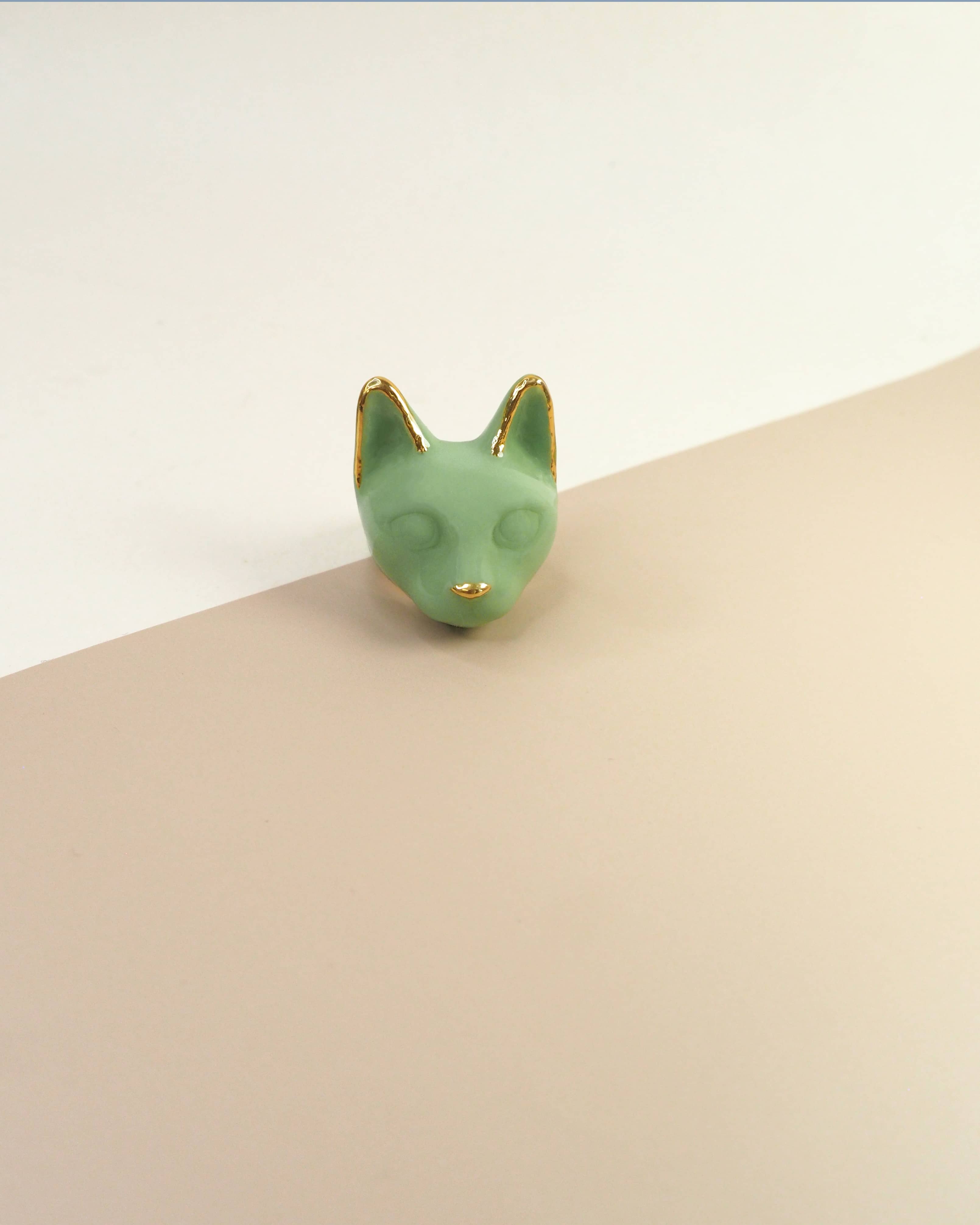 A green cathead ring with gold accents on the ears and a small gold nose placed on natural color background.