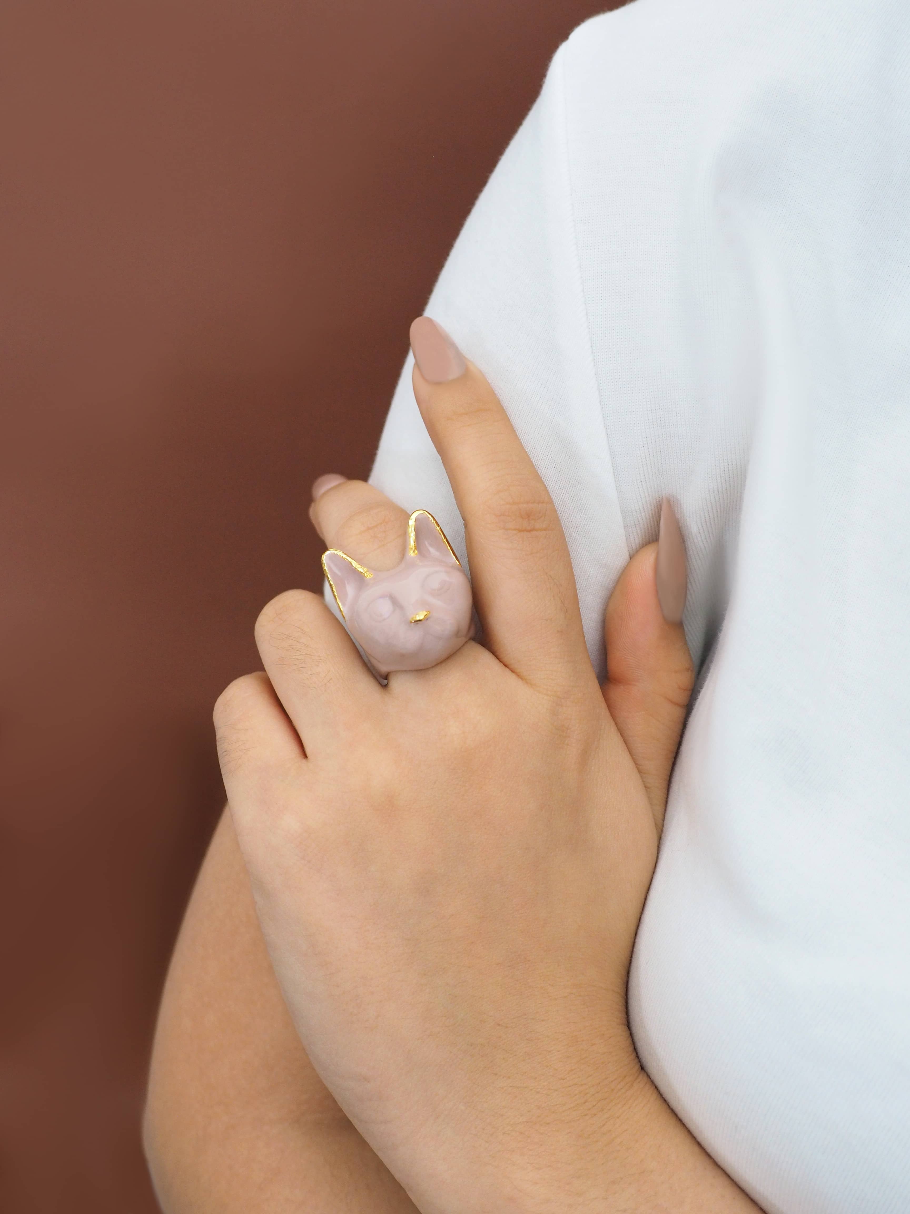 A dusty pink cat ring worn on a finger with casual outfit.