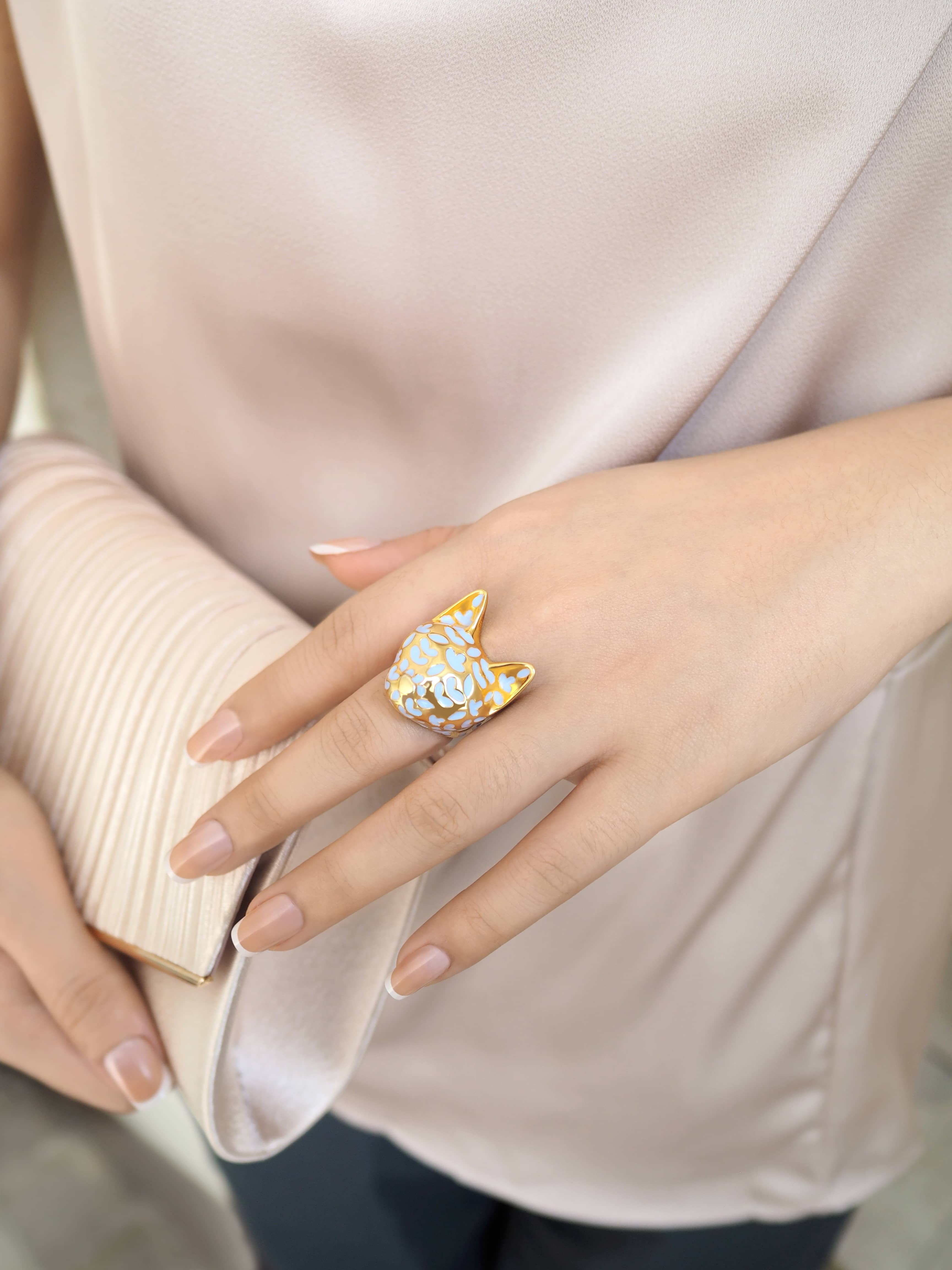 A hand adorned with a stylish cat-themed ring, showcasing elegance, while holding a clutch bag.