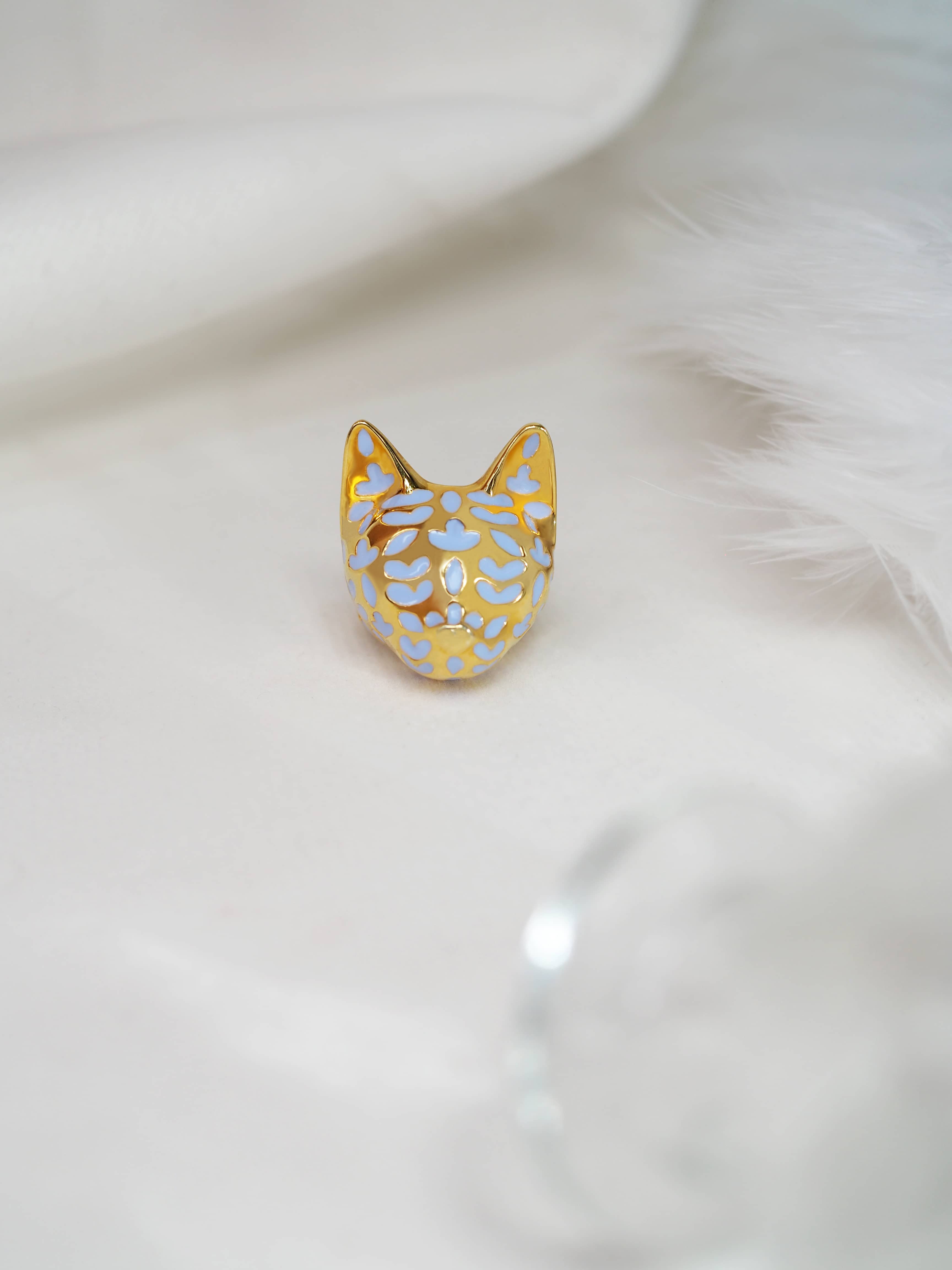 Elegant gold cat ring with lavender-inspired design placed on white fabric.