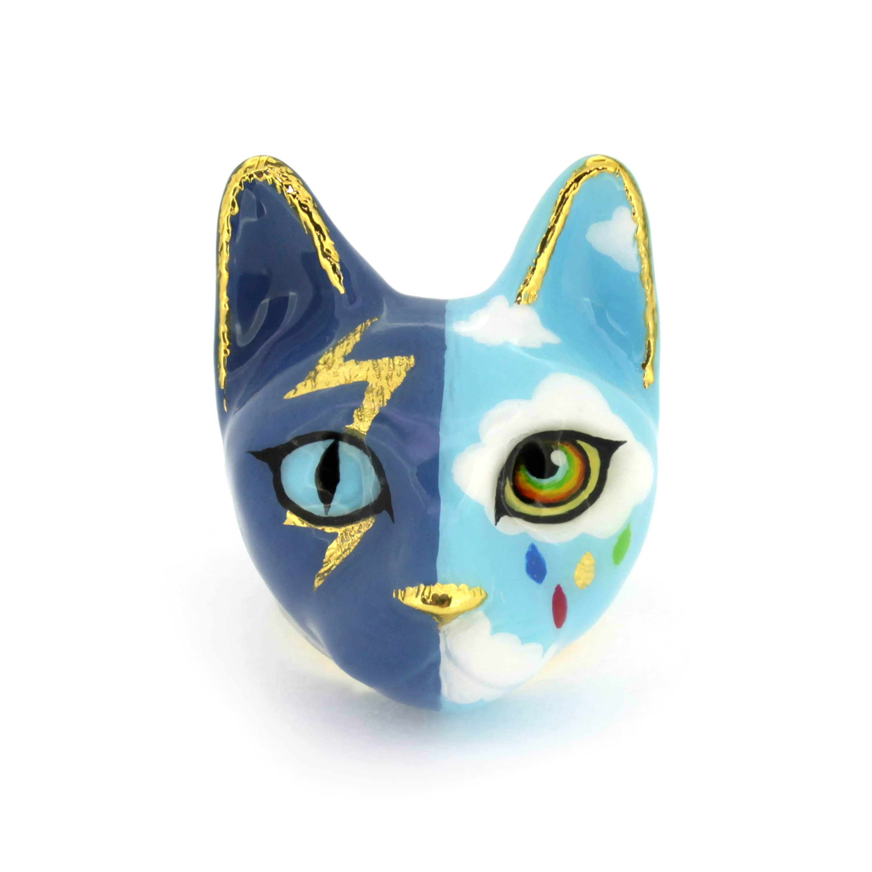A handcrafted cat ring with an artistic split-face design—half stormy skies with lightning, half bright skies with clouds and a rainbow.