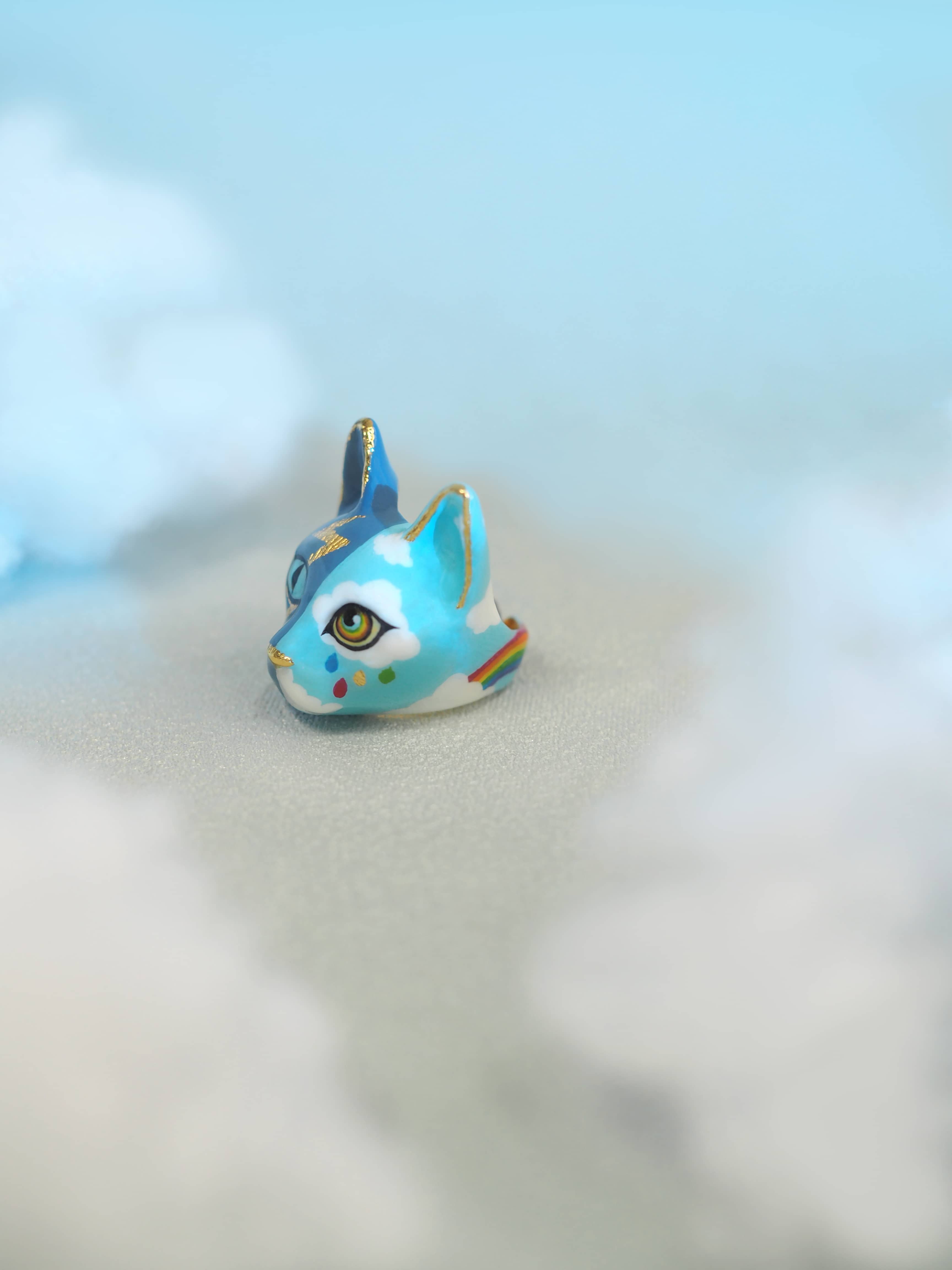 A whimsical cat ring design with hand-painted elements of thunder, clouds, and a rainbow.