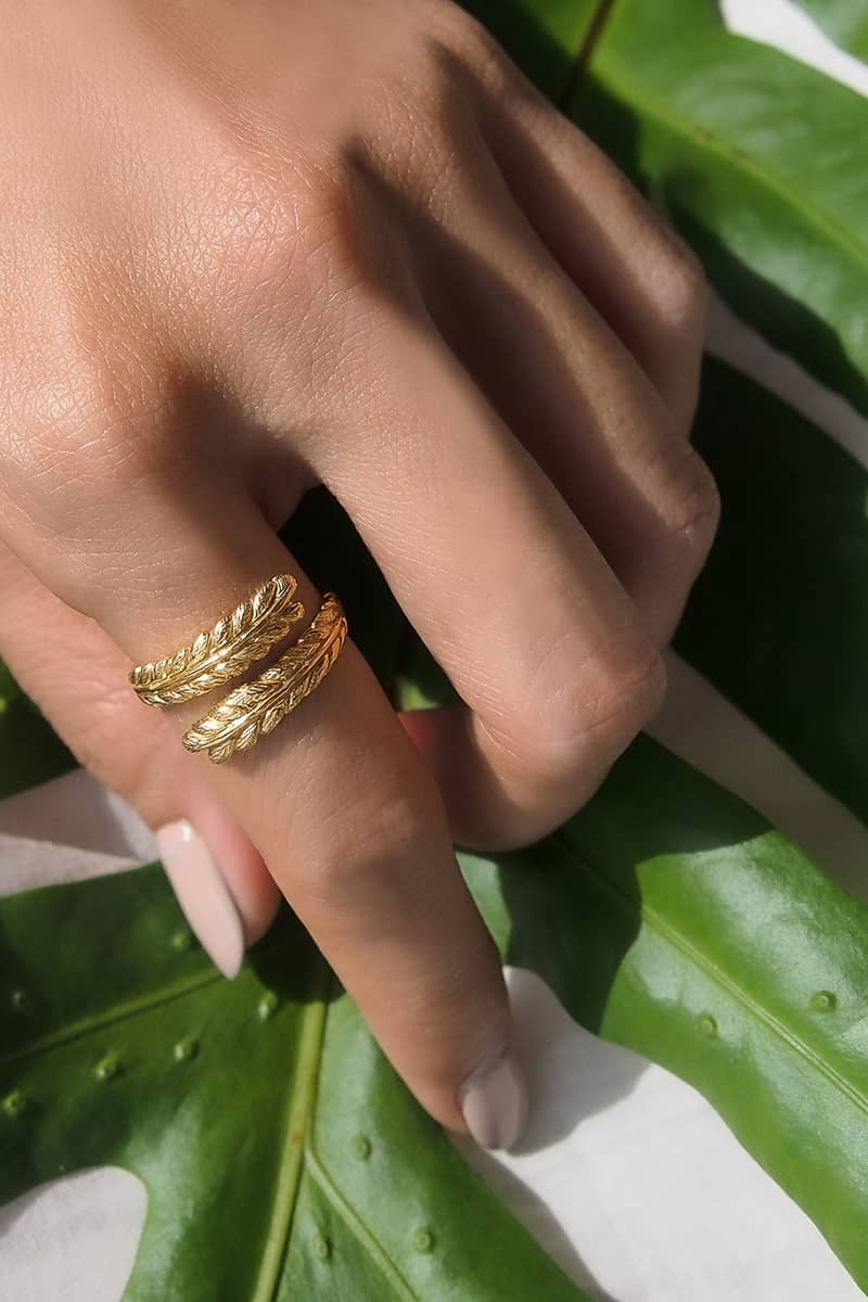 Close-up of a hand wearing twisted gold leaf ring on a green leaf background.