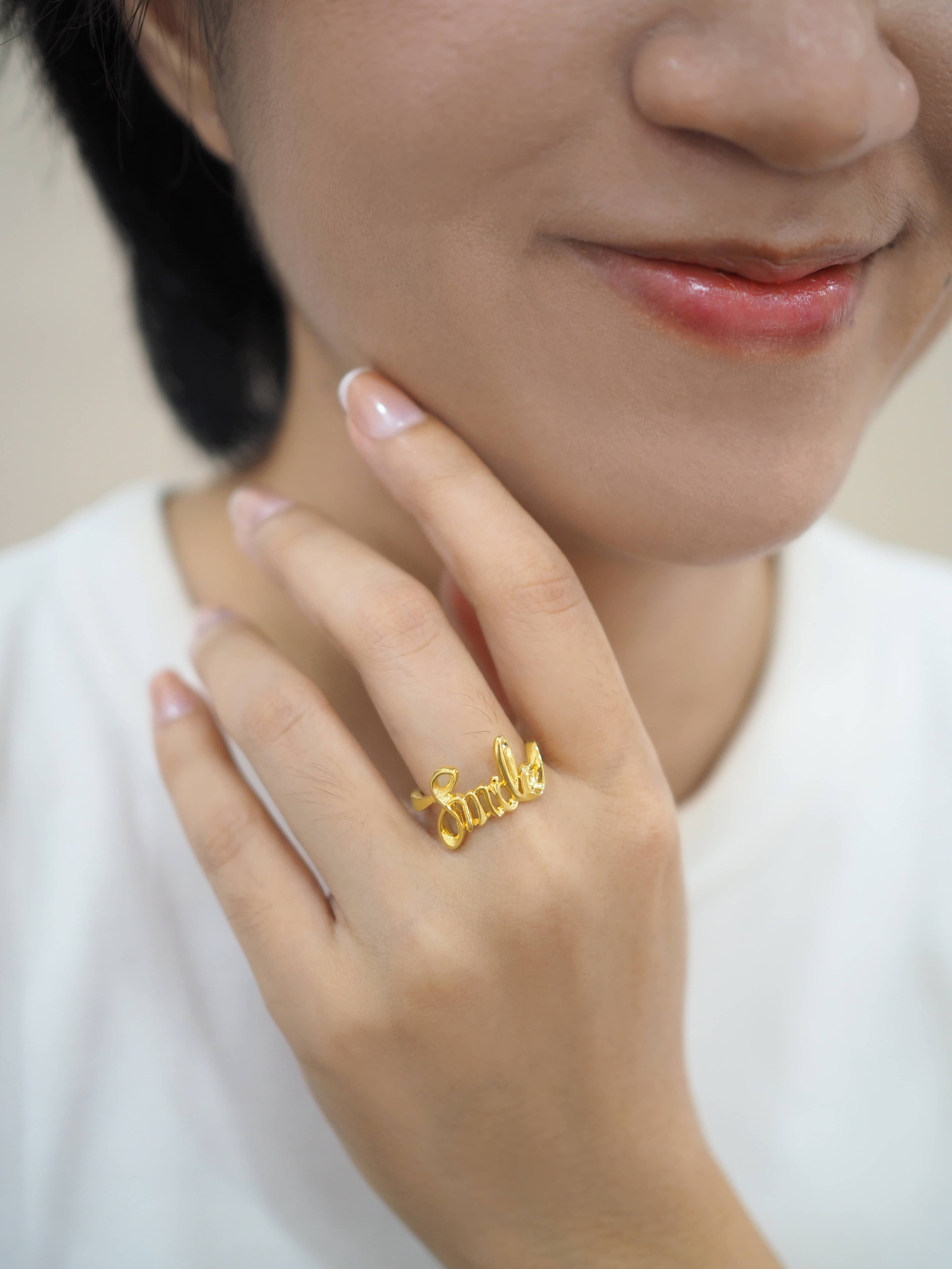 Close-up of a hand wearing a gold ring with the word 'smile'