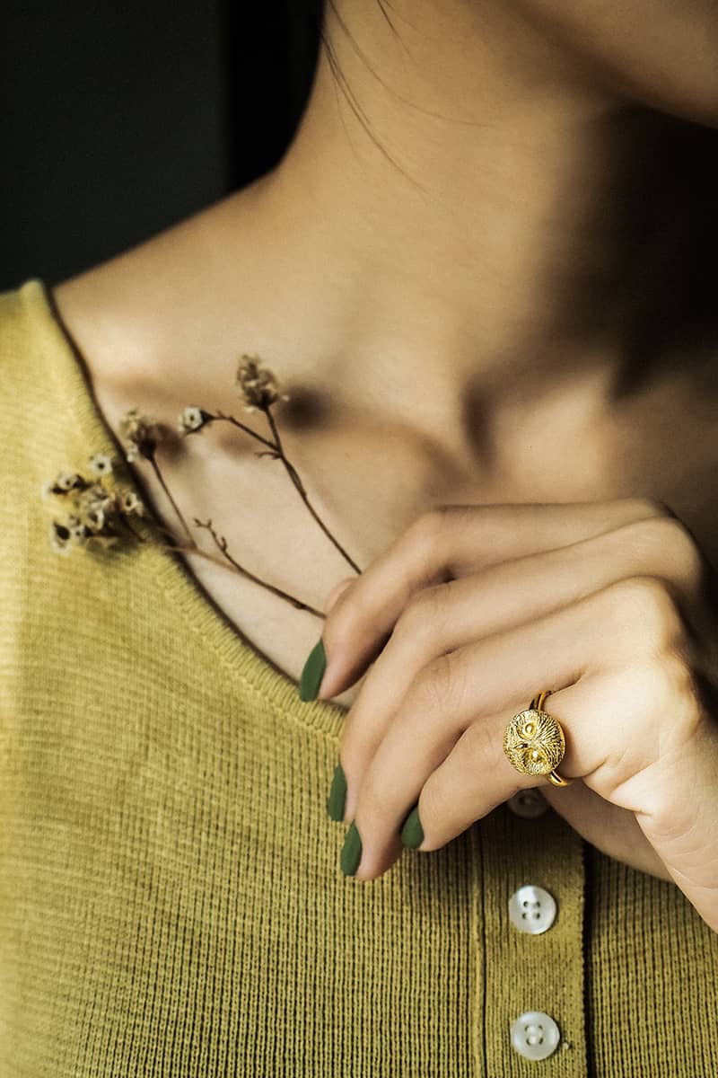 Detailed view of a stylish gold owl ring on a hand with flowers.