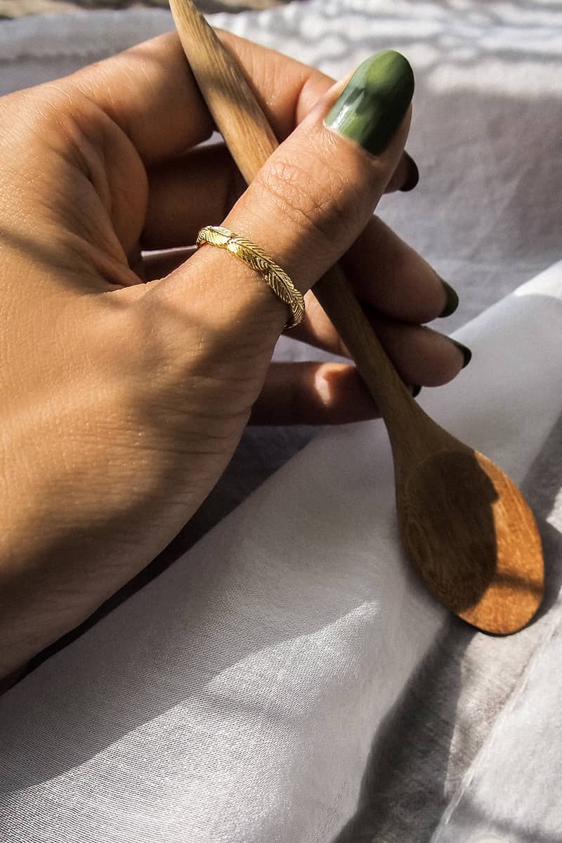 A close-up of a hand holding a wooden spoon, adorned with an elegant gold ring featuring feather design.