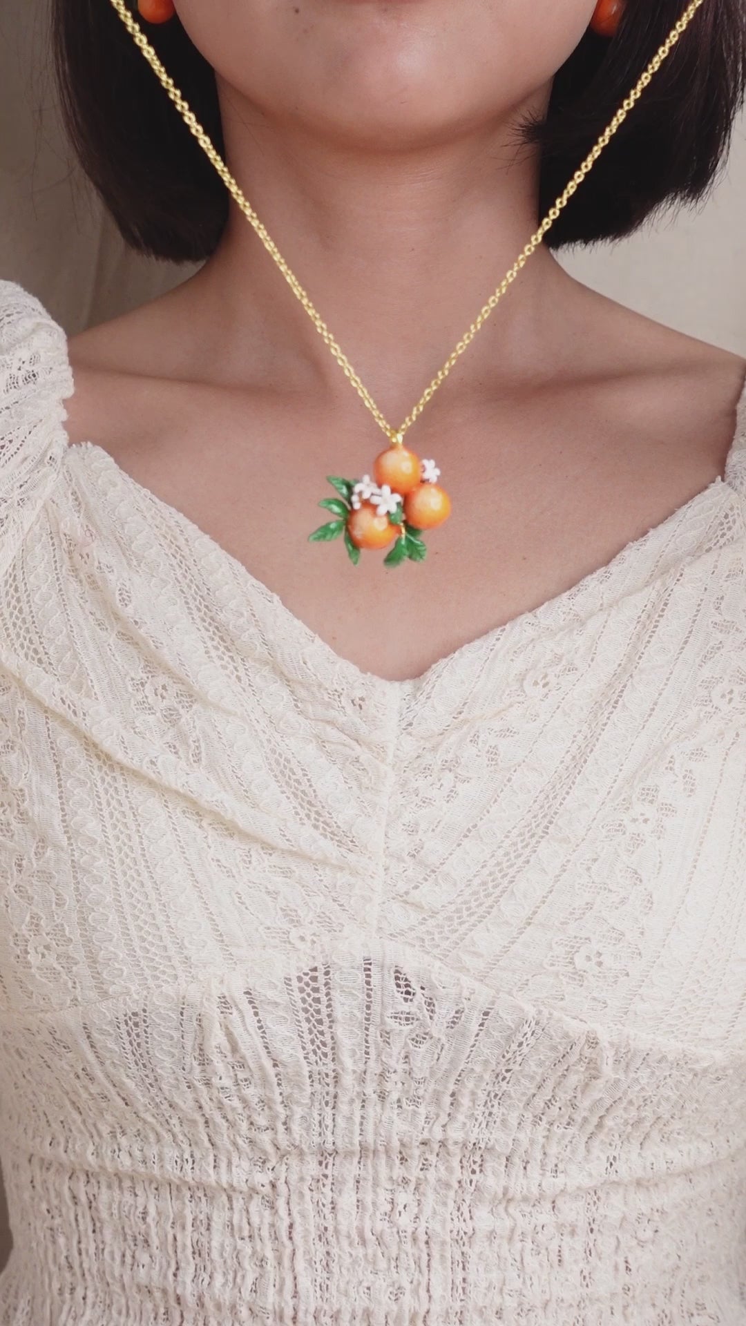 A close-up of a person wearing a gold chain necklace with orange charm and white flower accents, in a summer outfit.