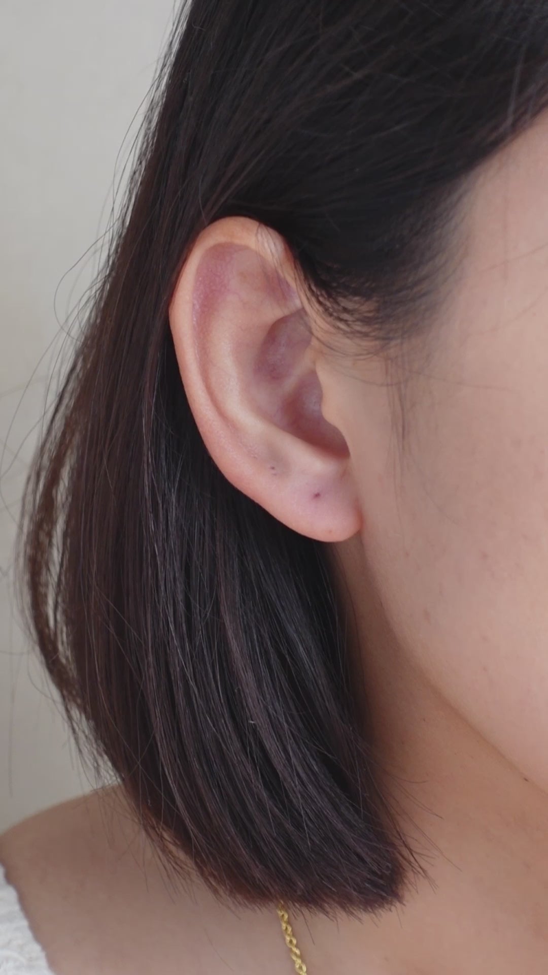 A close-up of an ear wearing charming orange earrings adorned with white flowers and green leaves.