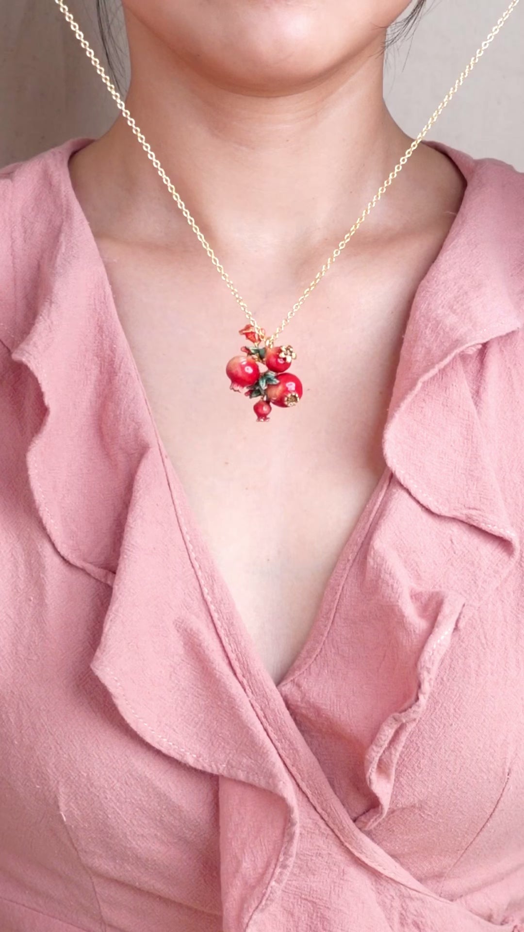 A close-up of a person wearing a gold chain necklace with pomegranate charms and green leaves accents, ideal for summer fashion.