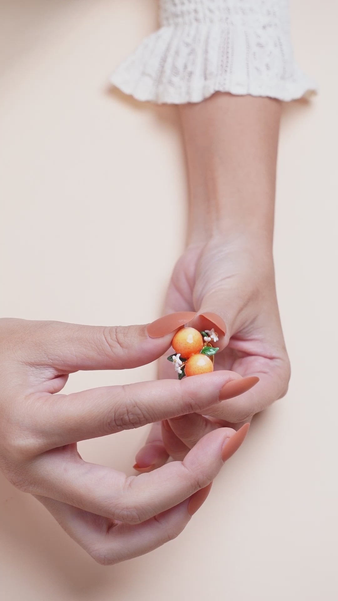 A hand wearing a handmade ring featuring two oranges, green leaves, and small white flowers, in a summer outfit.